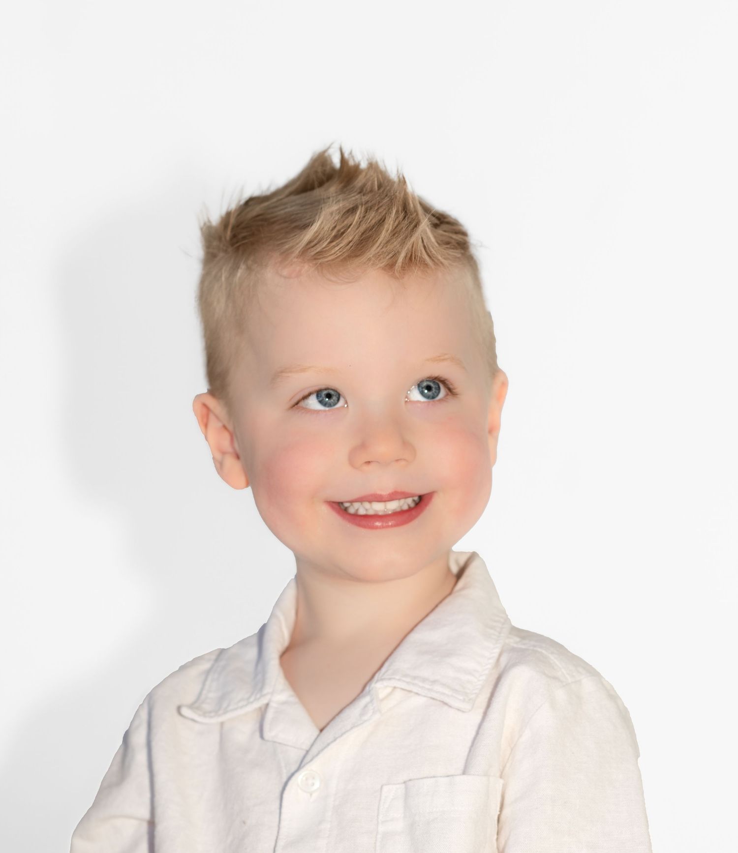 Young child with spiky blonde hair smiles while wearing white collared shirt against white background.