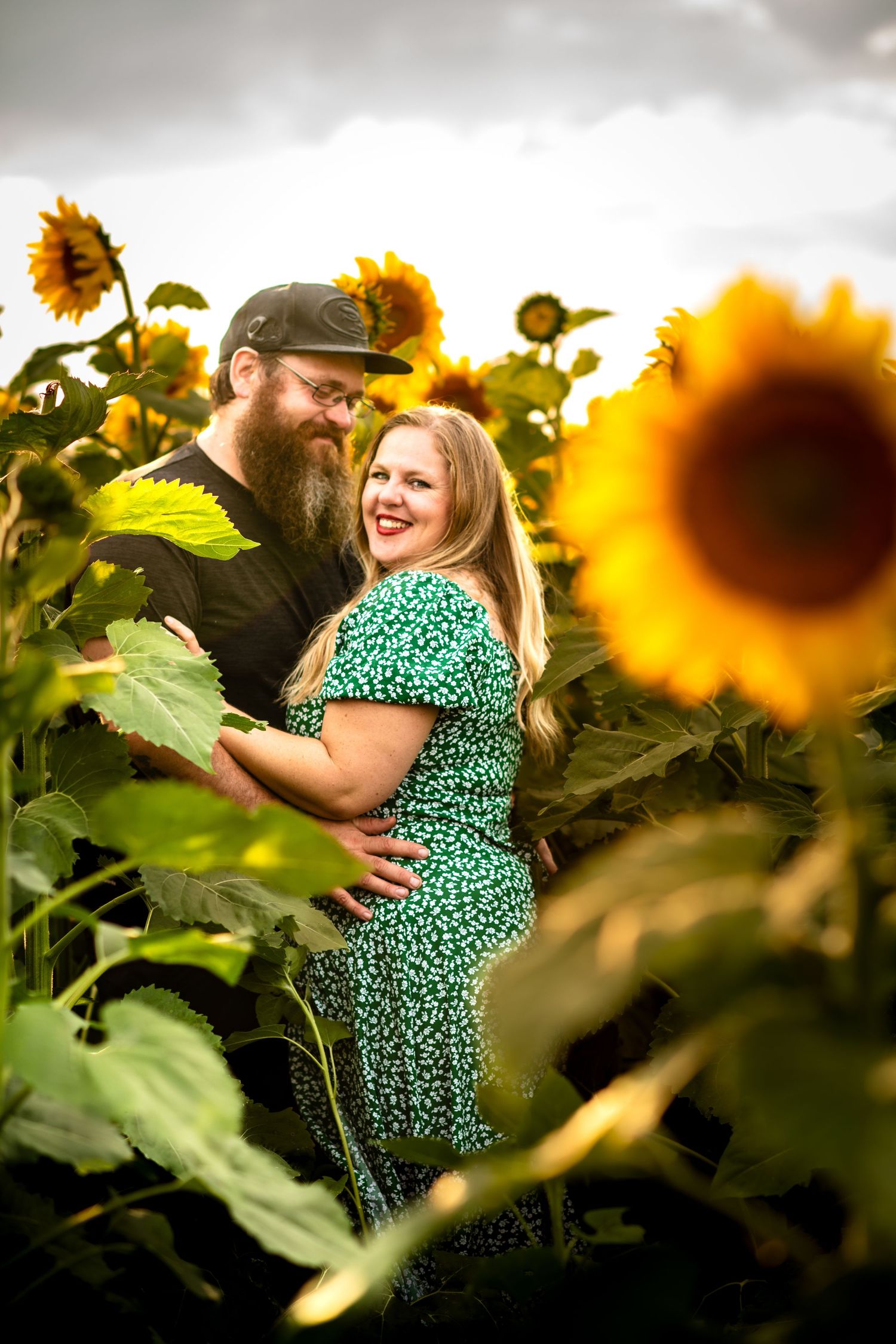 A romantic couple embraces while standing in a vibrant sunflower field during golden hour.