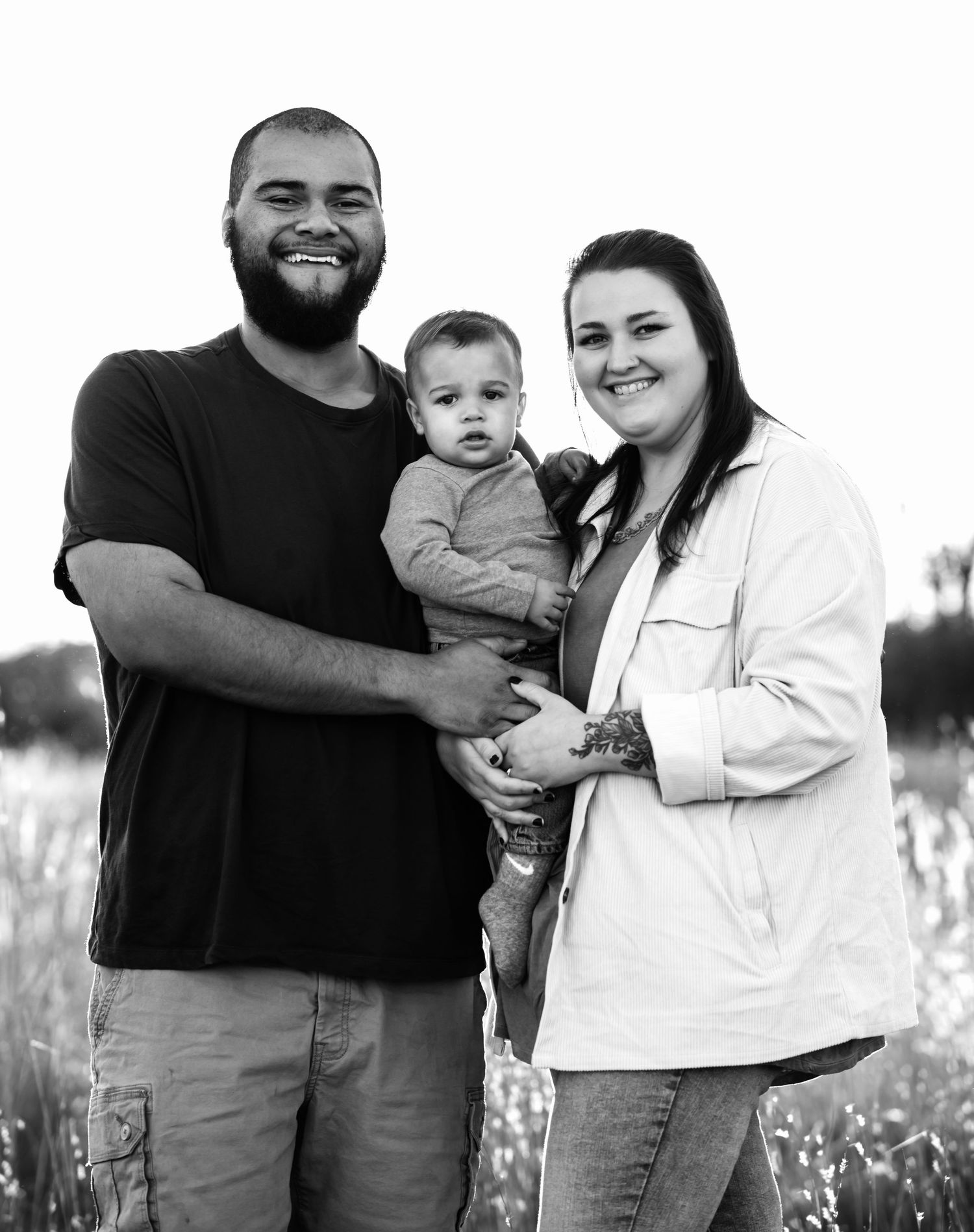 A family poses together outdoors for a black and white portrait in a field.