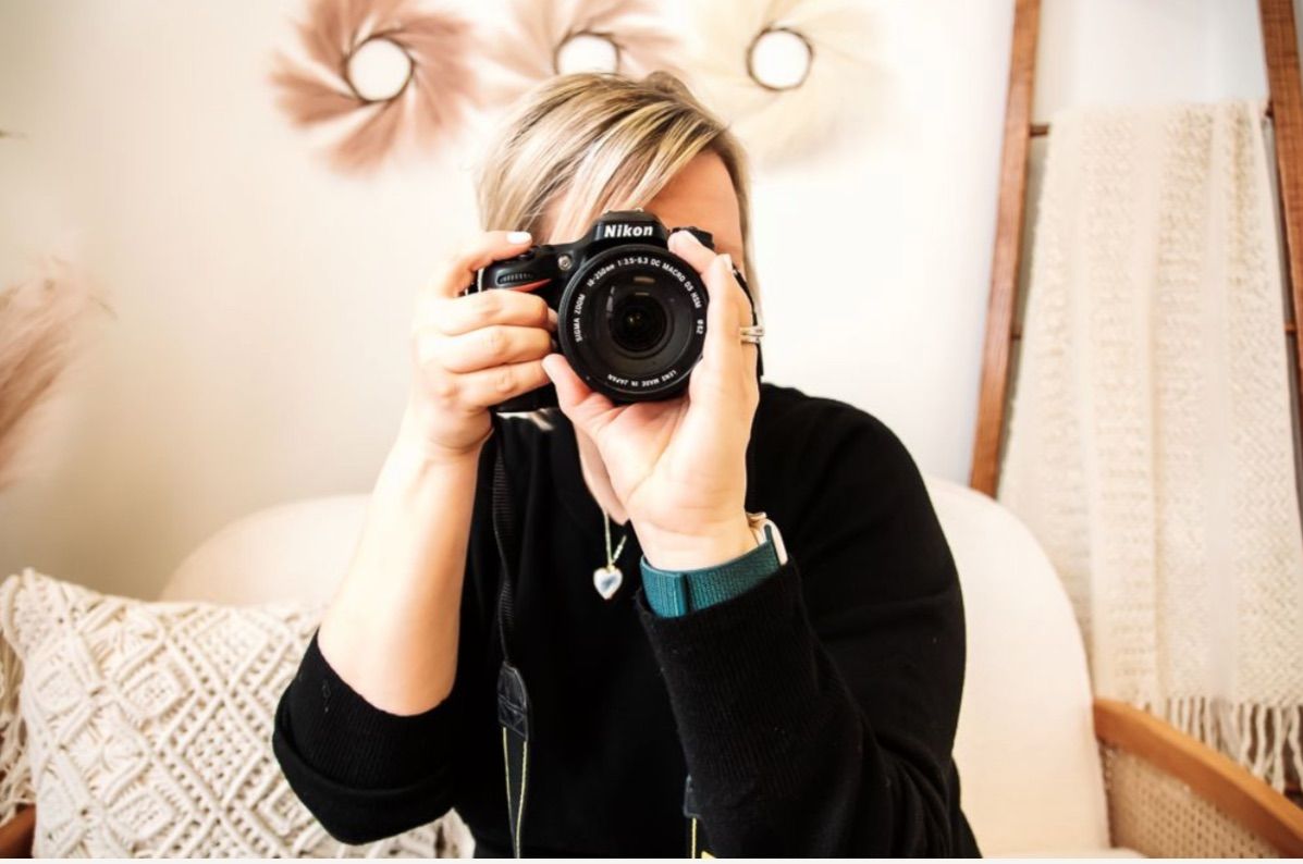 Person holding professional camera while taking photo in cozy room with warm lighting.
