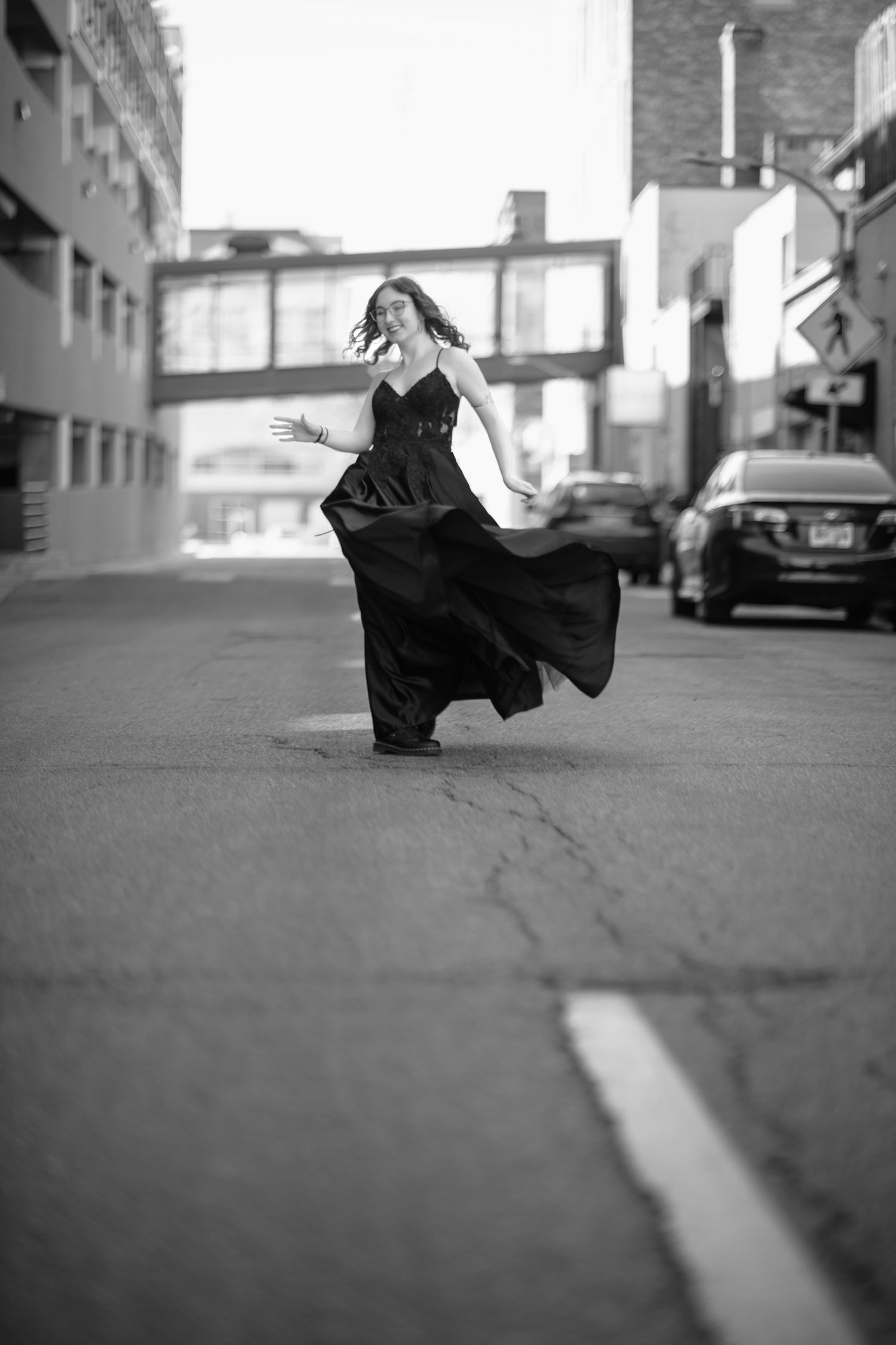 A person in a flowing black dress dances in an urban street setting captured in black and white.