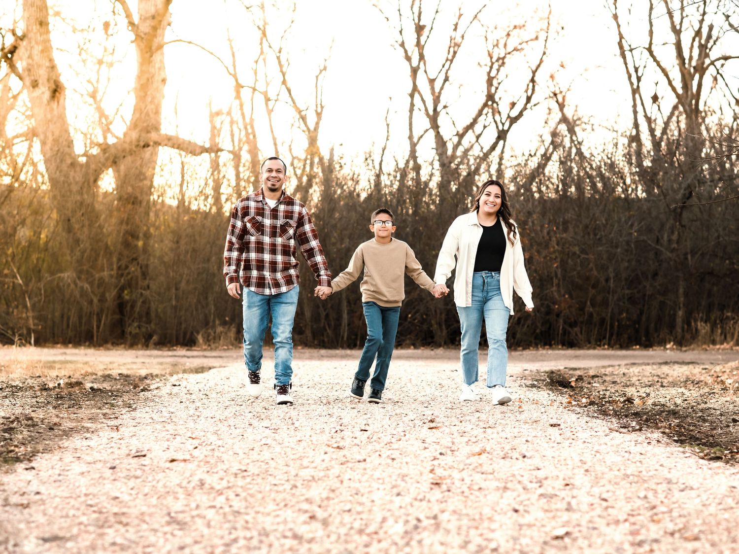 Family walks together on path during sunset with bare trees in background.