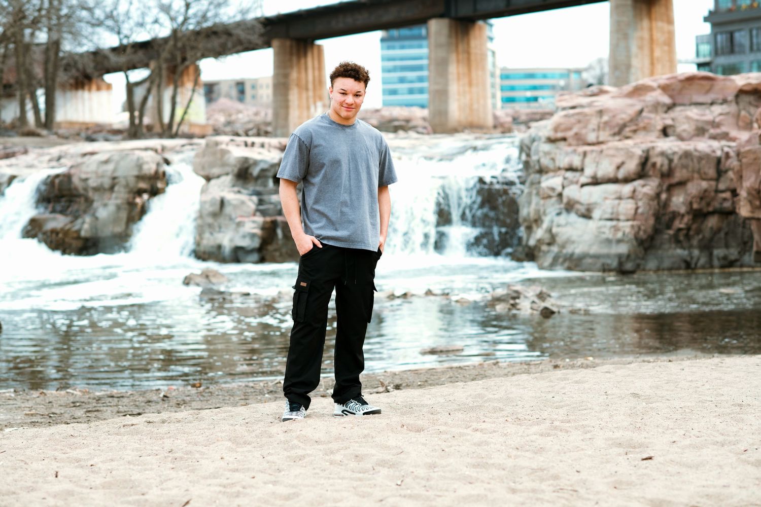 Person standing in front of scenic waterfall and rocks wearing casual attire.