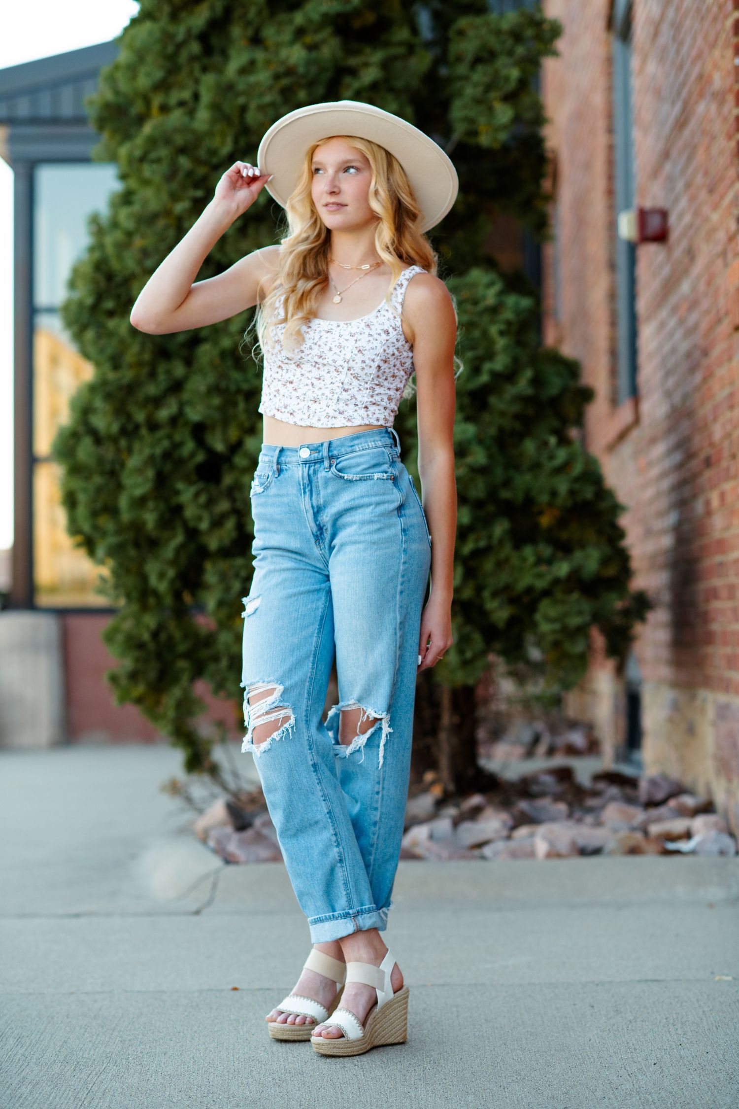 Summer fashion with cropped lace top, distressed boyfriend jeans, wide brim hat and platform sandals on urban sidewalk.