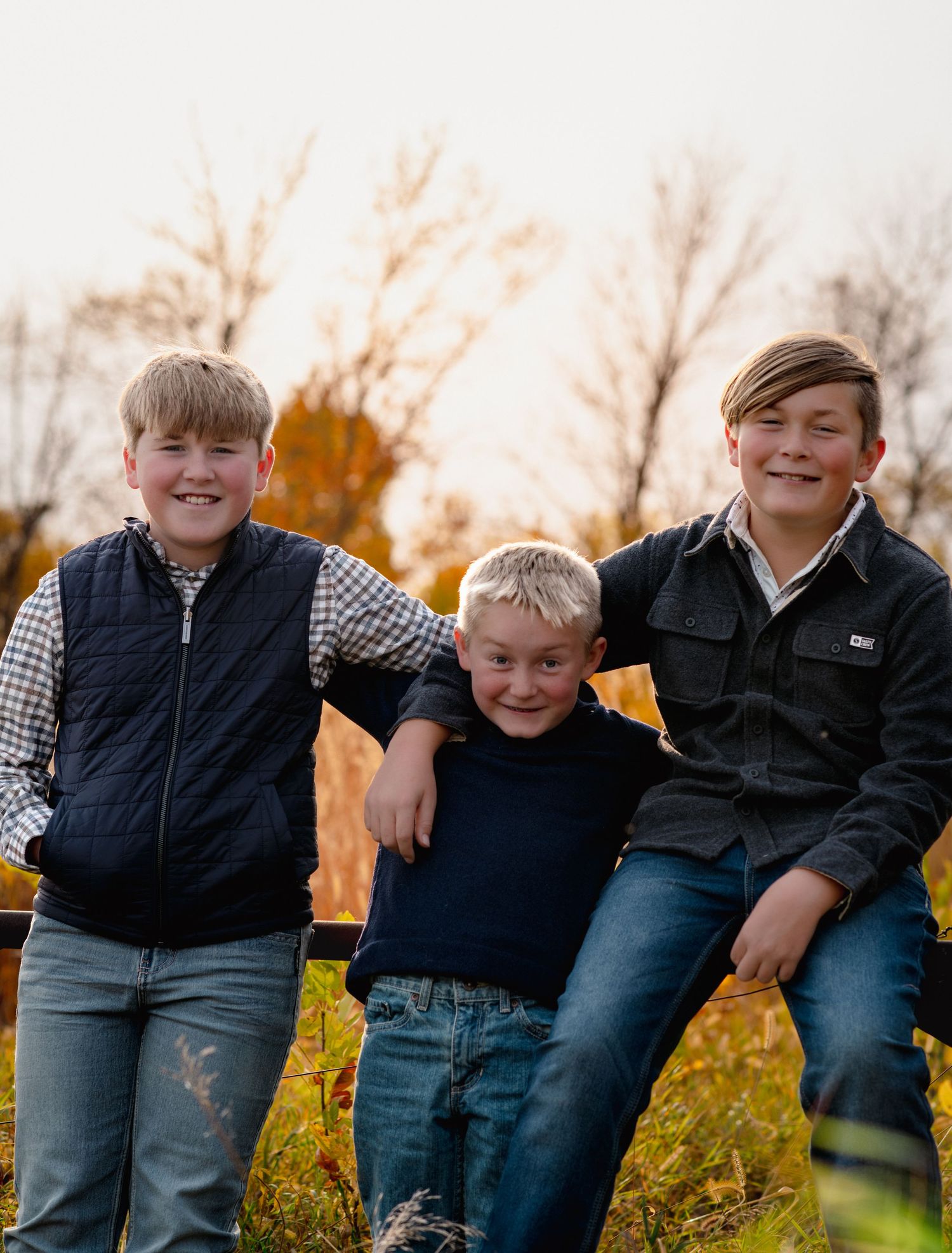 Three brothers share a joyful moment together on a fence during autumn.