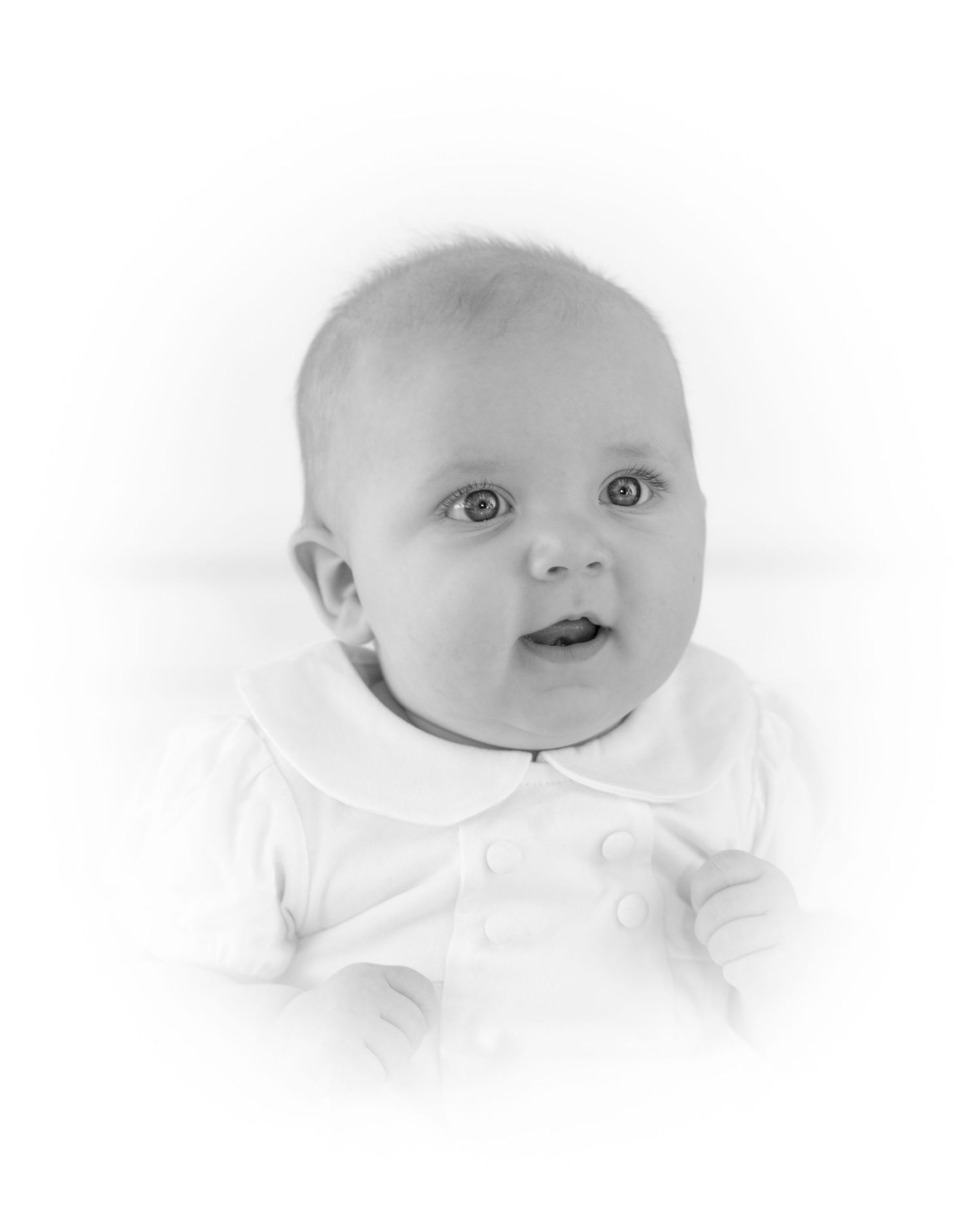 Black and white portrait of an infant wearing white clothing against light background.