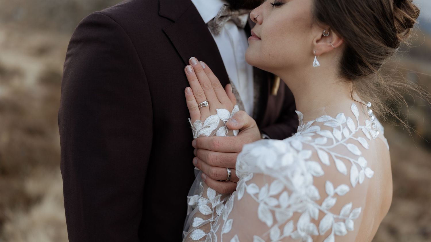 Close-up wedding elopement detail of bride and groom holding hands, showing rings and lace dress texture in the Dolomites