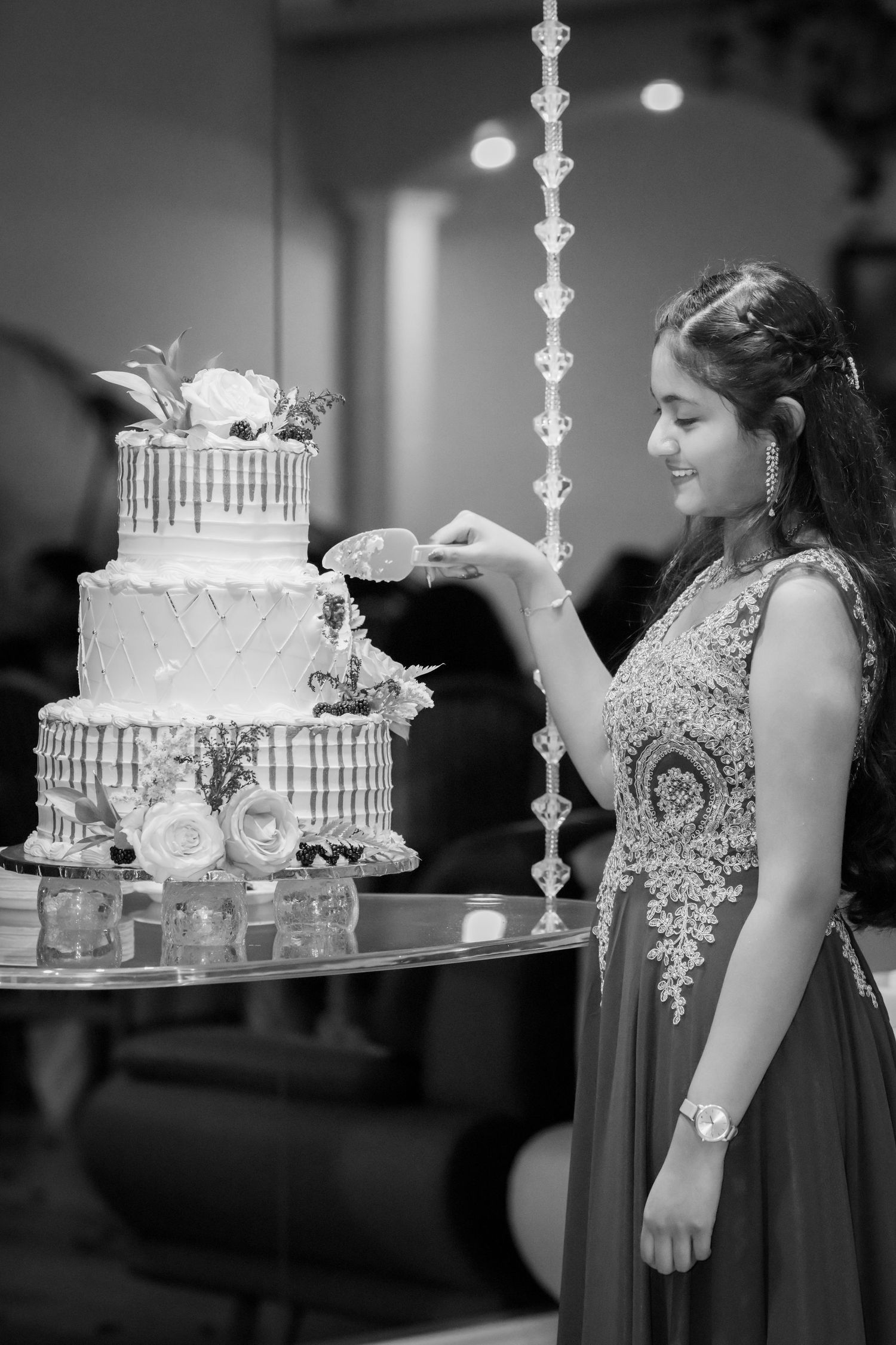 A person in an embellished gown cuts a three-tier white wedding cake with floral decorations.
