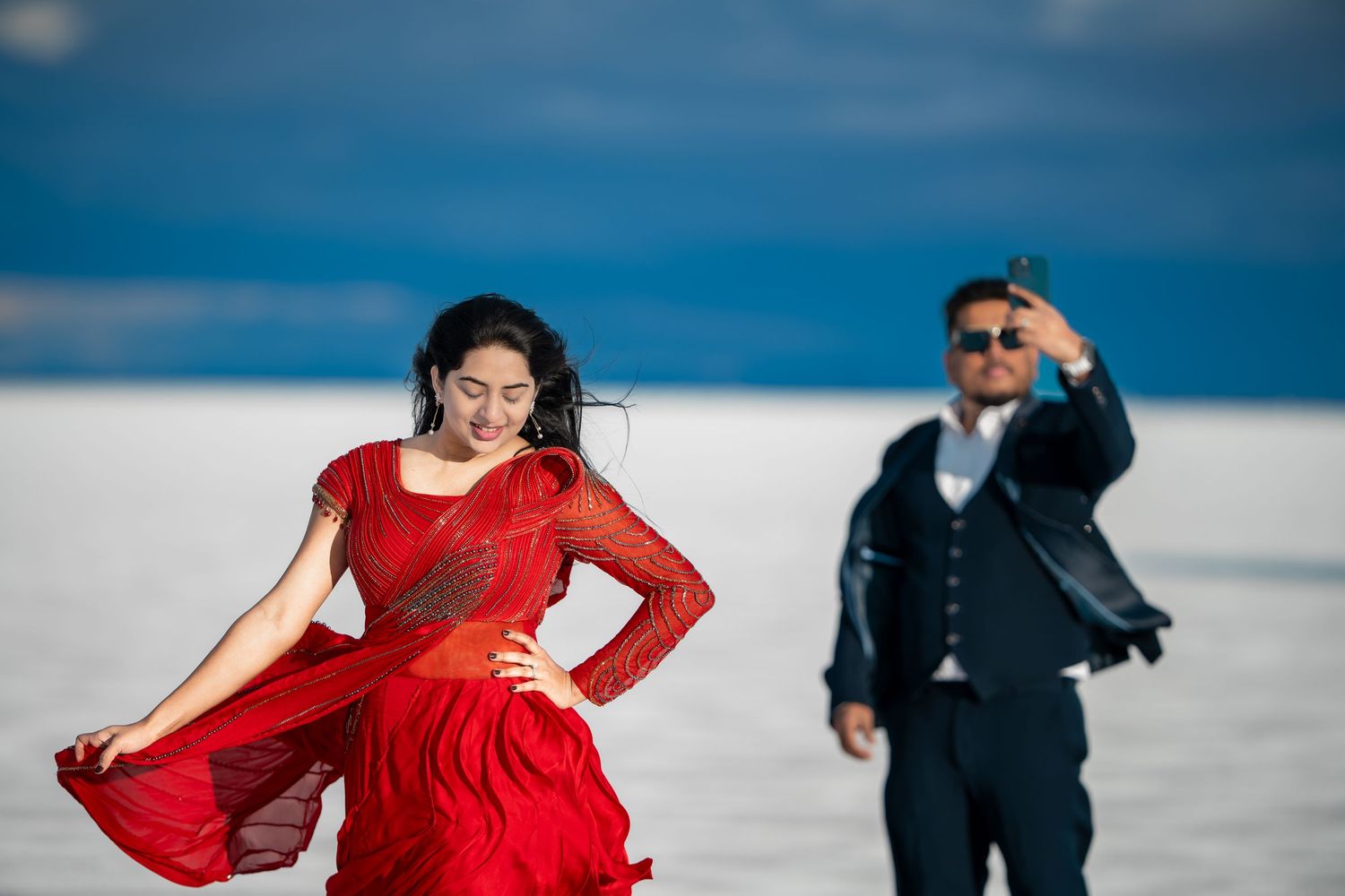 Woman in flowing red dress twirls on salt flats as companion watches.