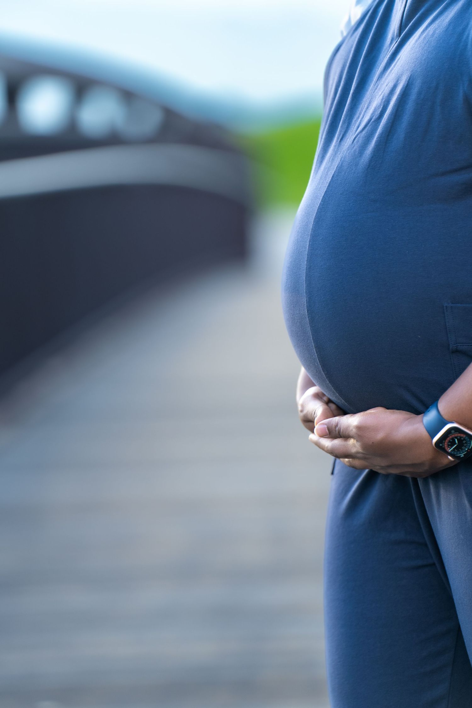 A side profile of a pregnant belly in a blue dress with hands gently cradling it.