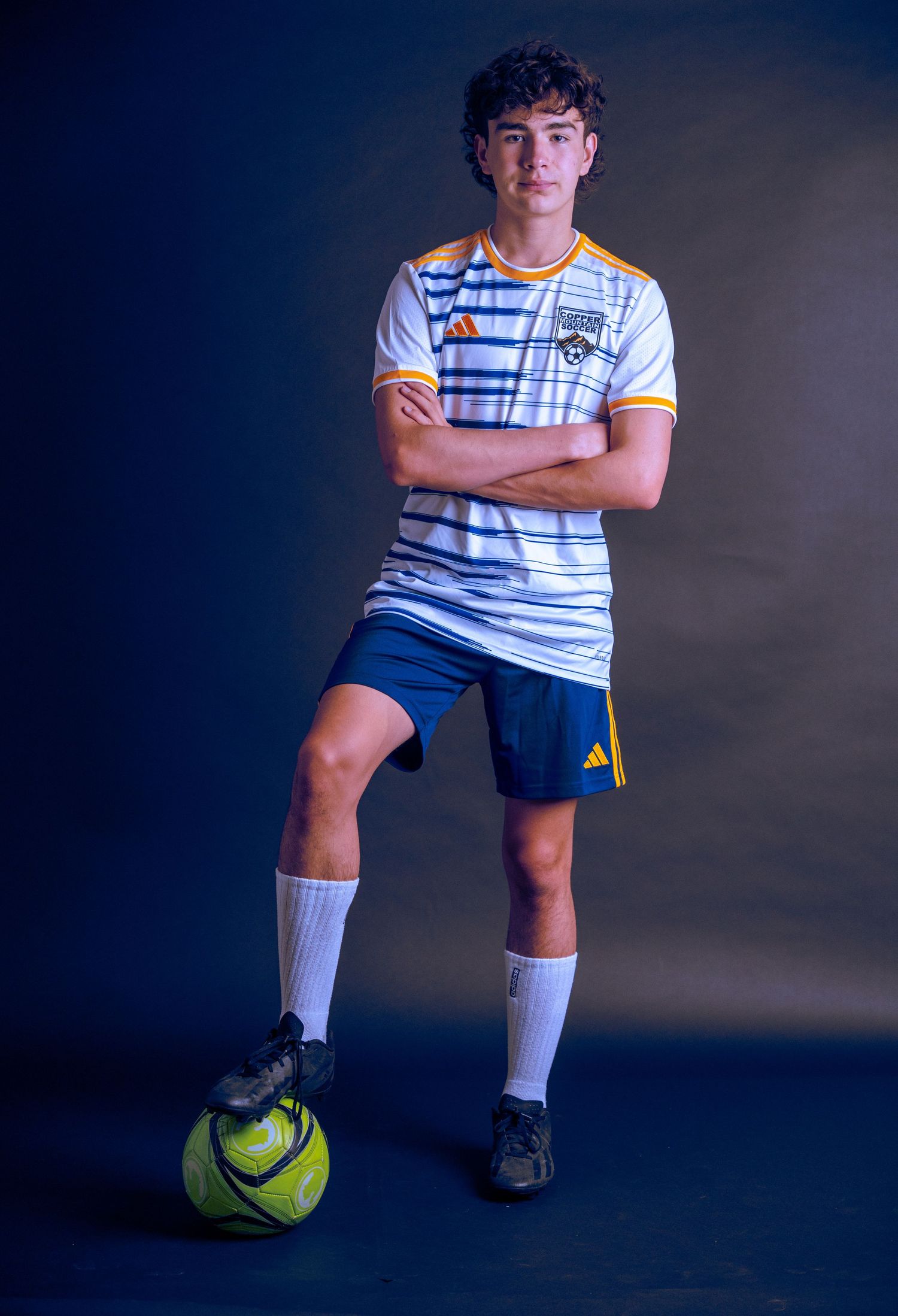 Soccer player in striped jersey poses with ball during studio photoshoot.
