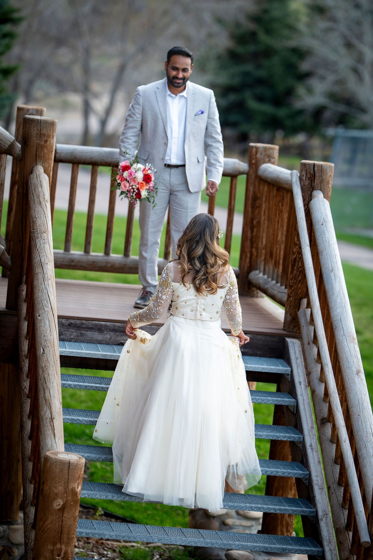 Romantic wedding moments captured at a rustic wooden fence with a couple in elegant white and gray attire.