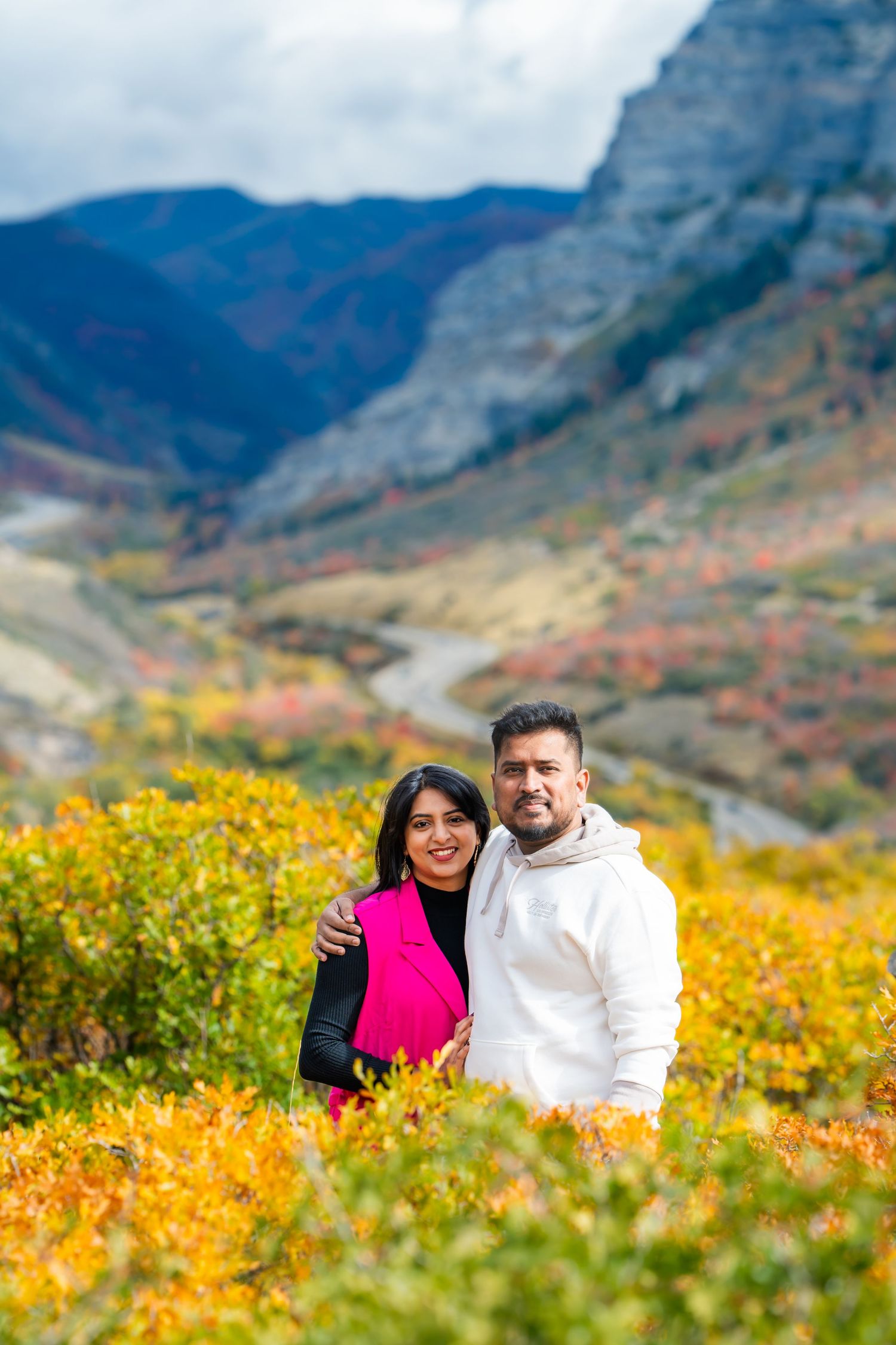 Couple embracing amid vibrant yellow wildflowers with mountain valley vista.