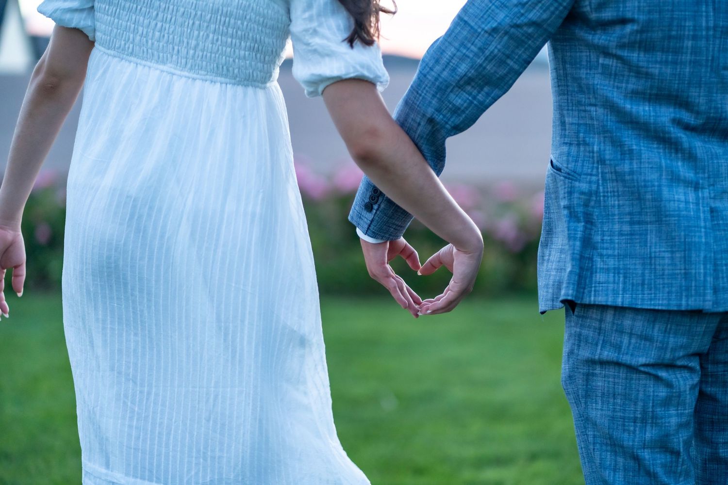 Two people holding hands together while walking on grass in blue and white outfits.