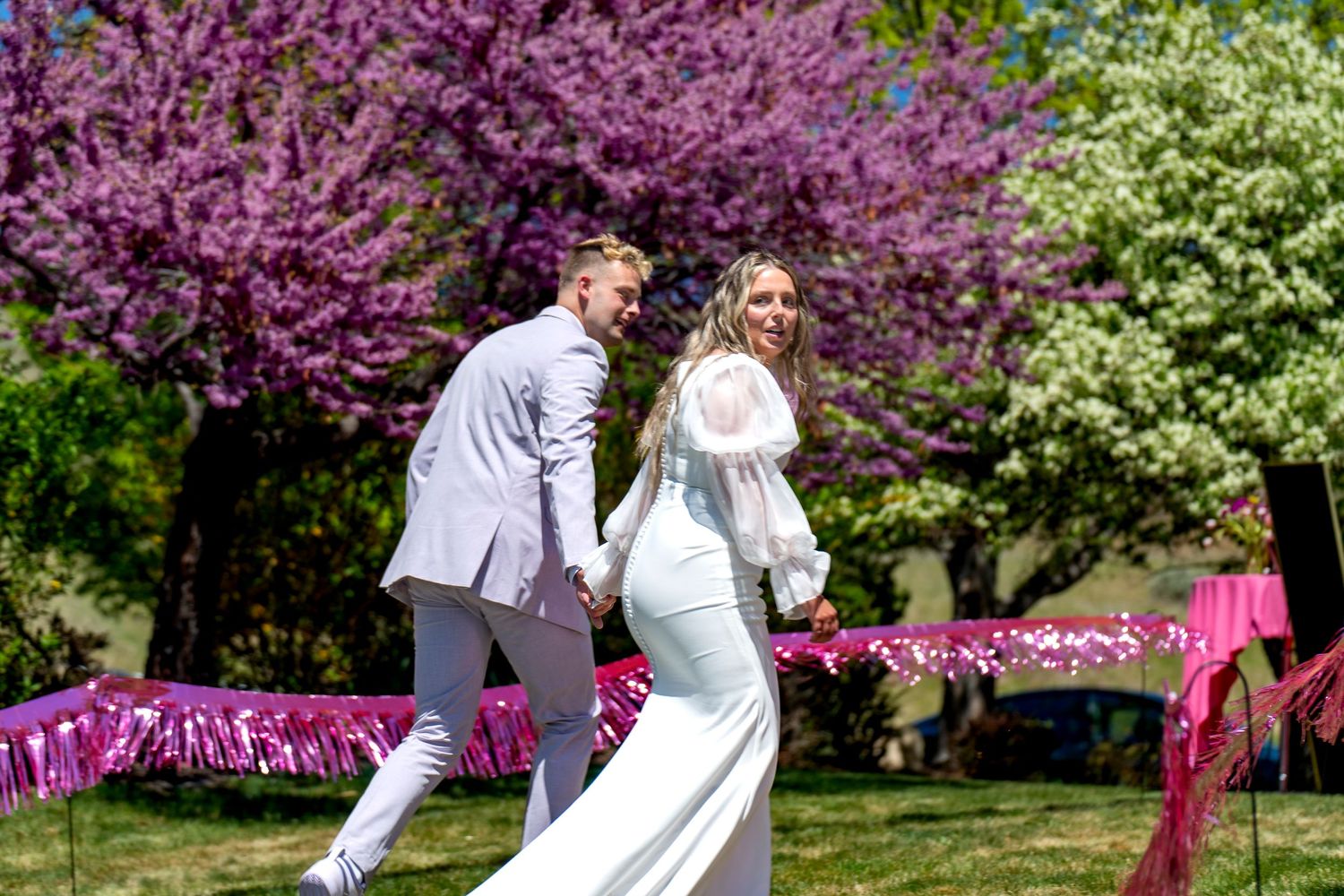 Newlyweds dancing under blooming cherry blossom trees with pink flower decorations.