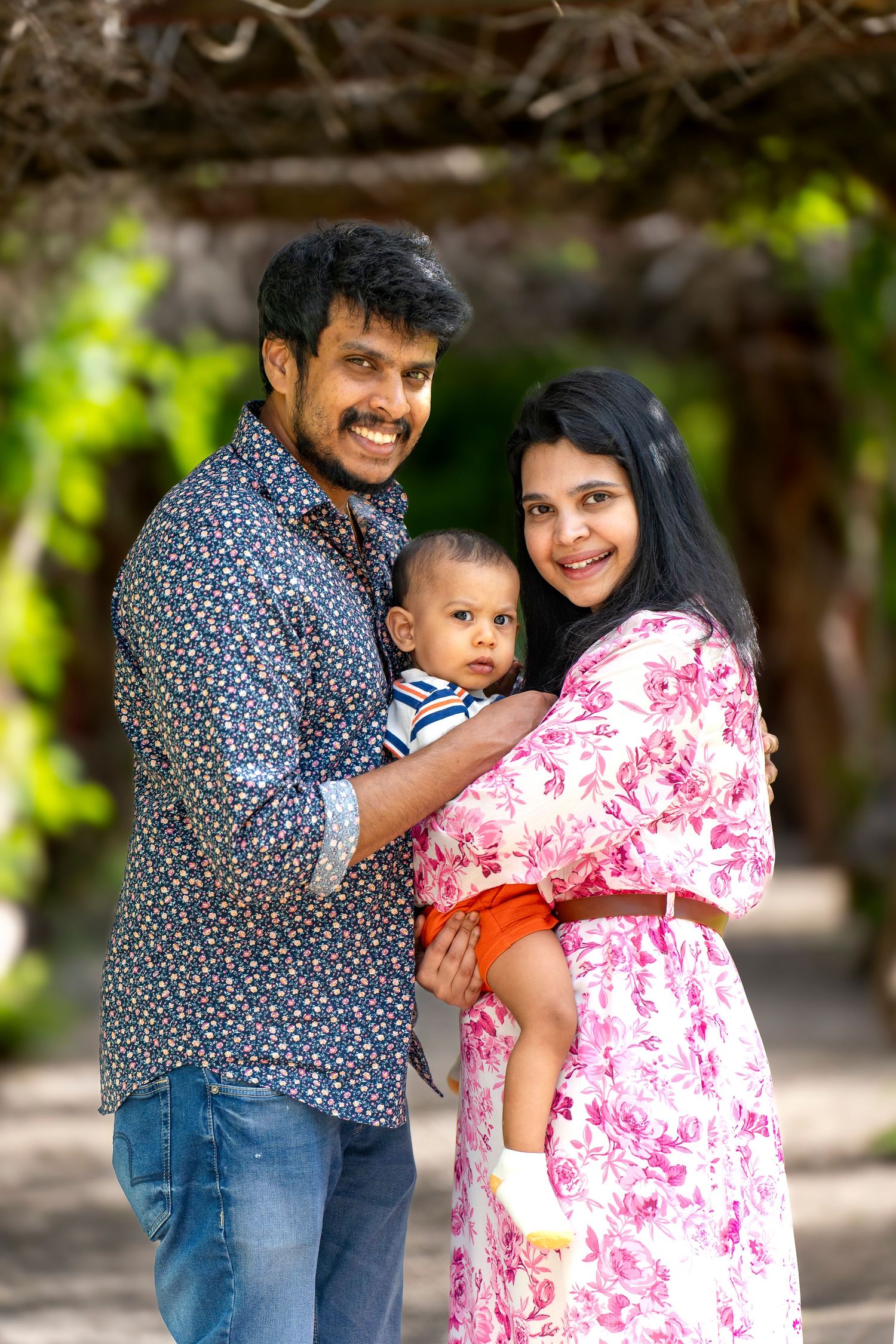 A family portrait taken outdoors with natural foliage in the background.