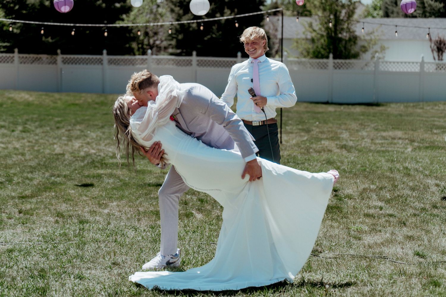 Romantic outdoor wedding scene with playful dip pose on grass lawn.