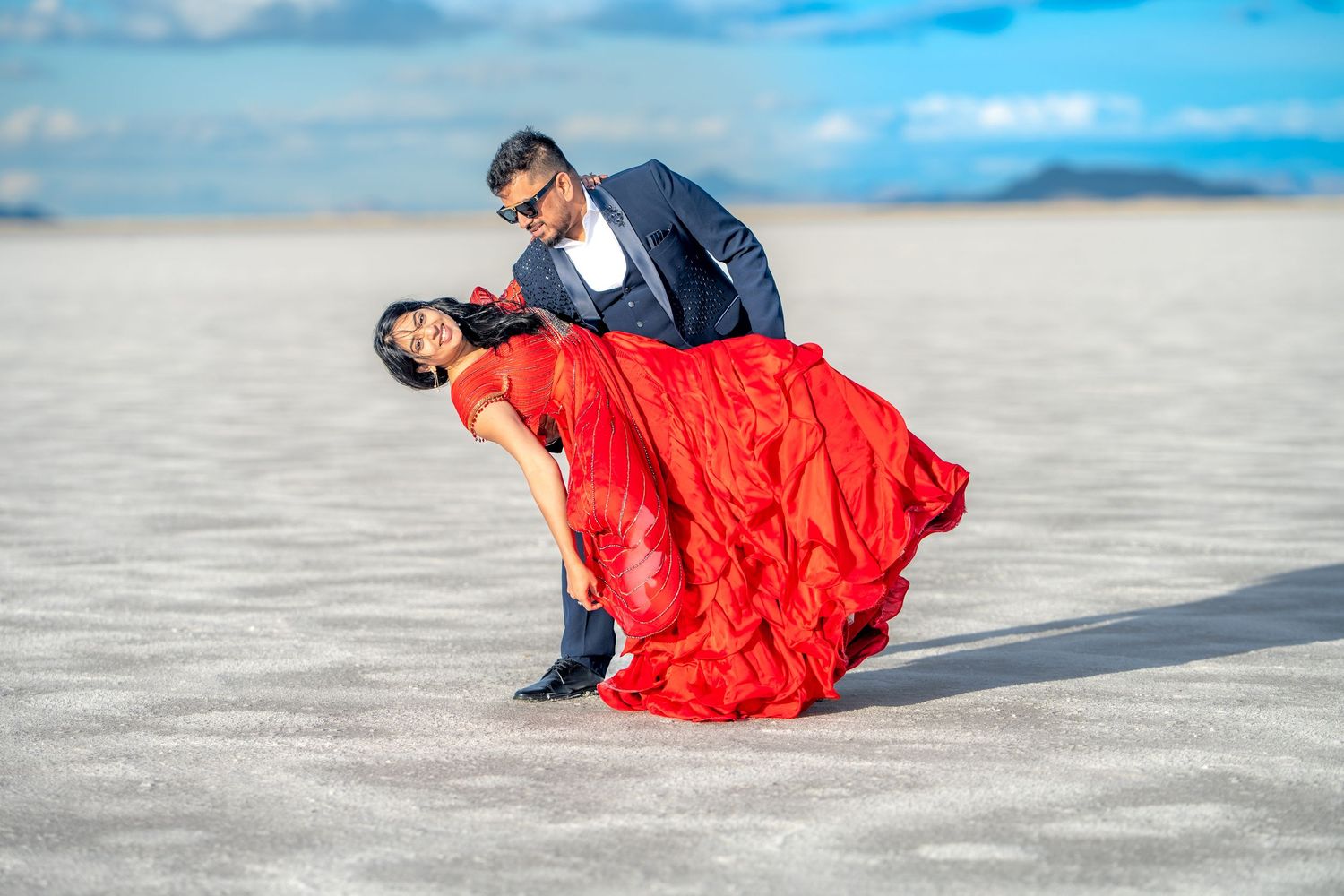 A romantic dance pose with a flowing red dress on a bright salt flat landscape.