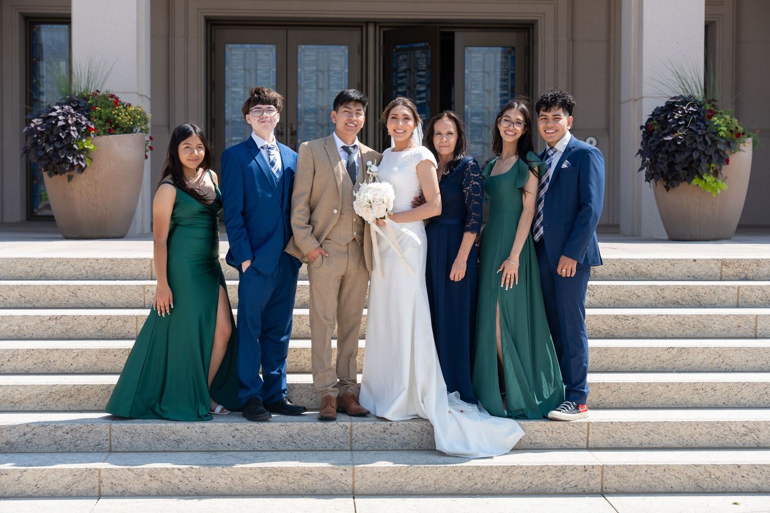 Wedding party poses on stone steps wearing coordinated green dresses and formal suits.