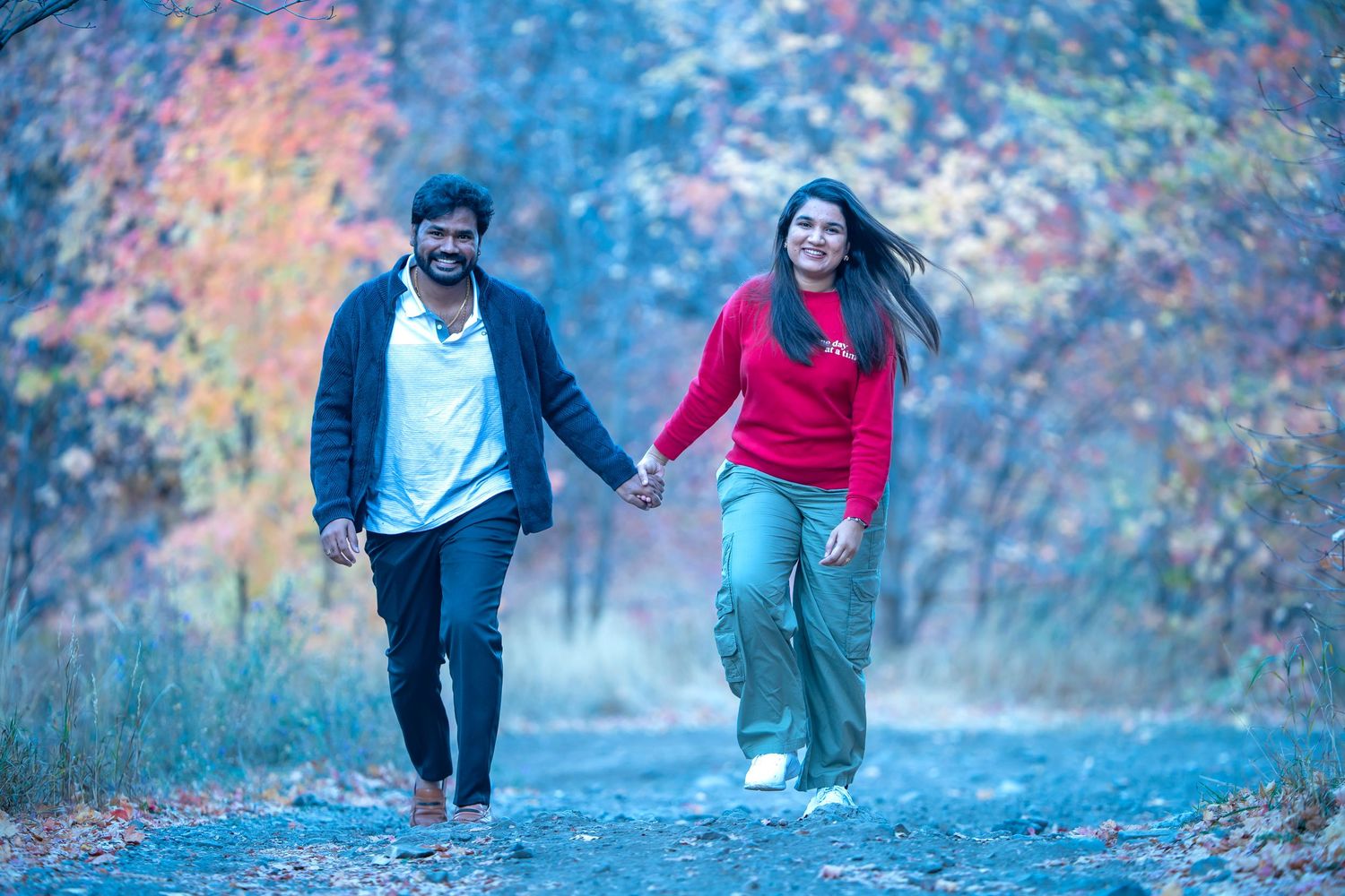 Couple walking hand in hand on trail with vibrant fall foliage.