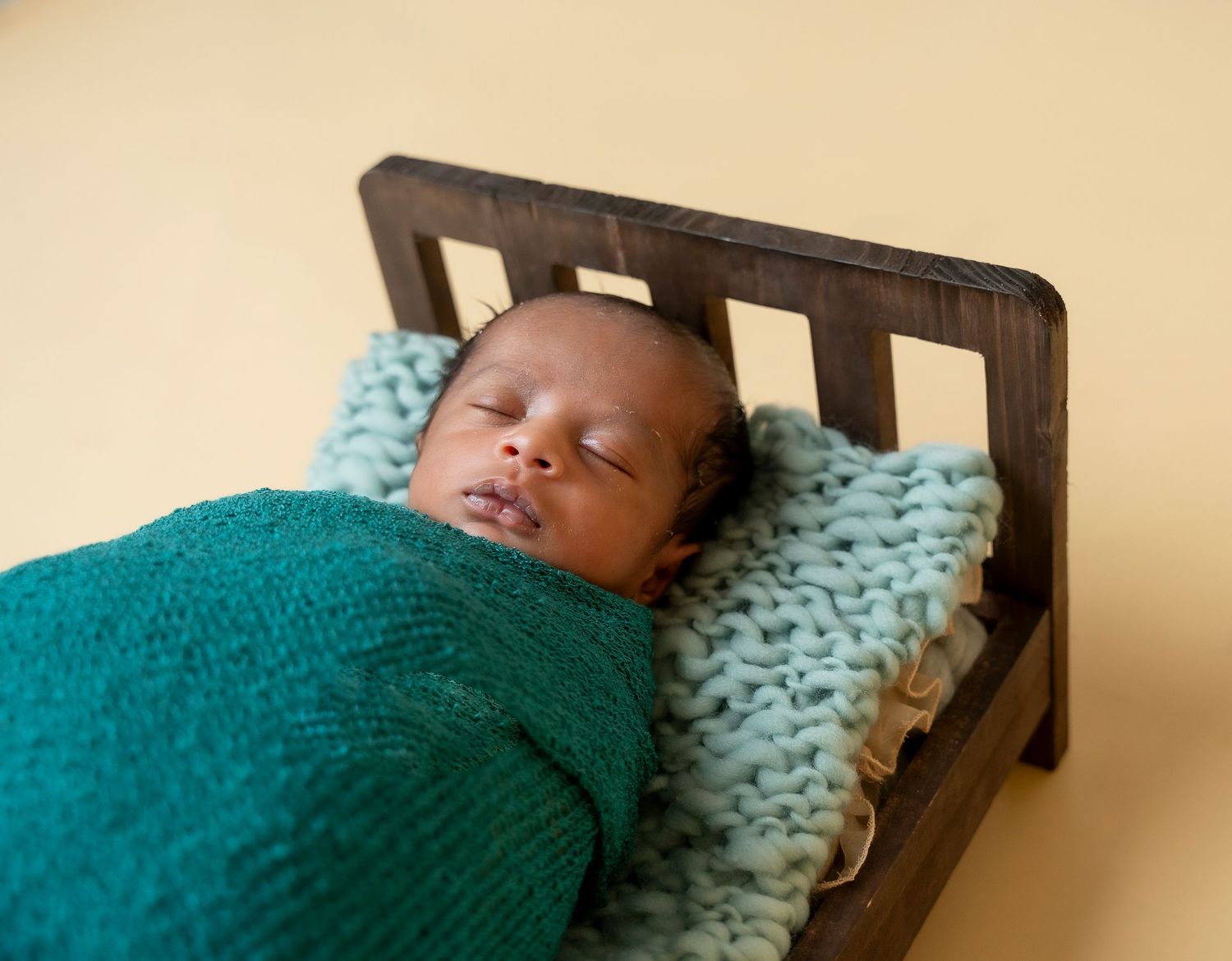 Sleeping baby wrapped in turquoise blanket rests peacefully in dark wooden crib.