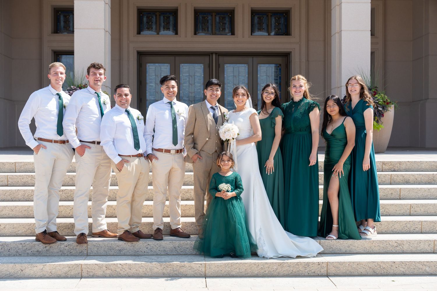Wedding party poses on stone steps in coordinated green dresses and khaki suits.
