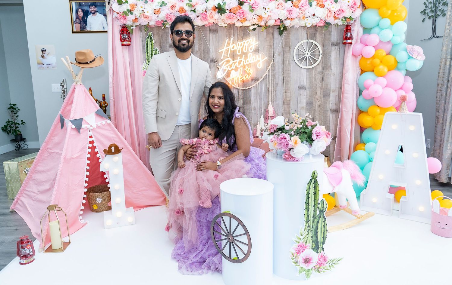 Family posing at western-themed party setup with balloon decorations and pink teepee.