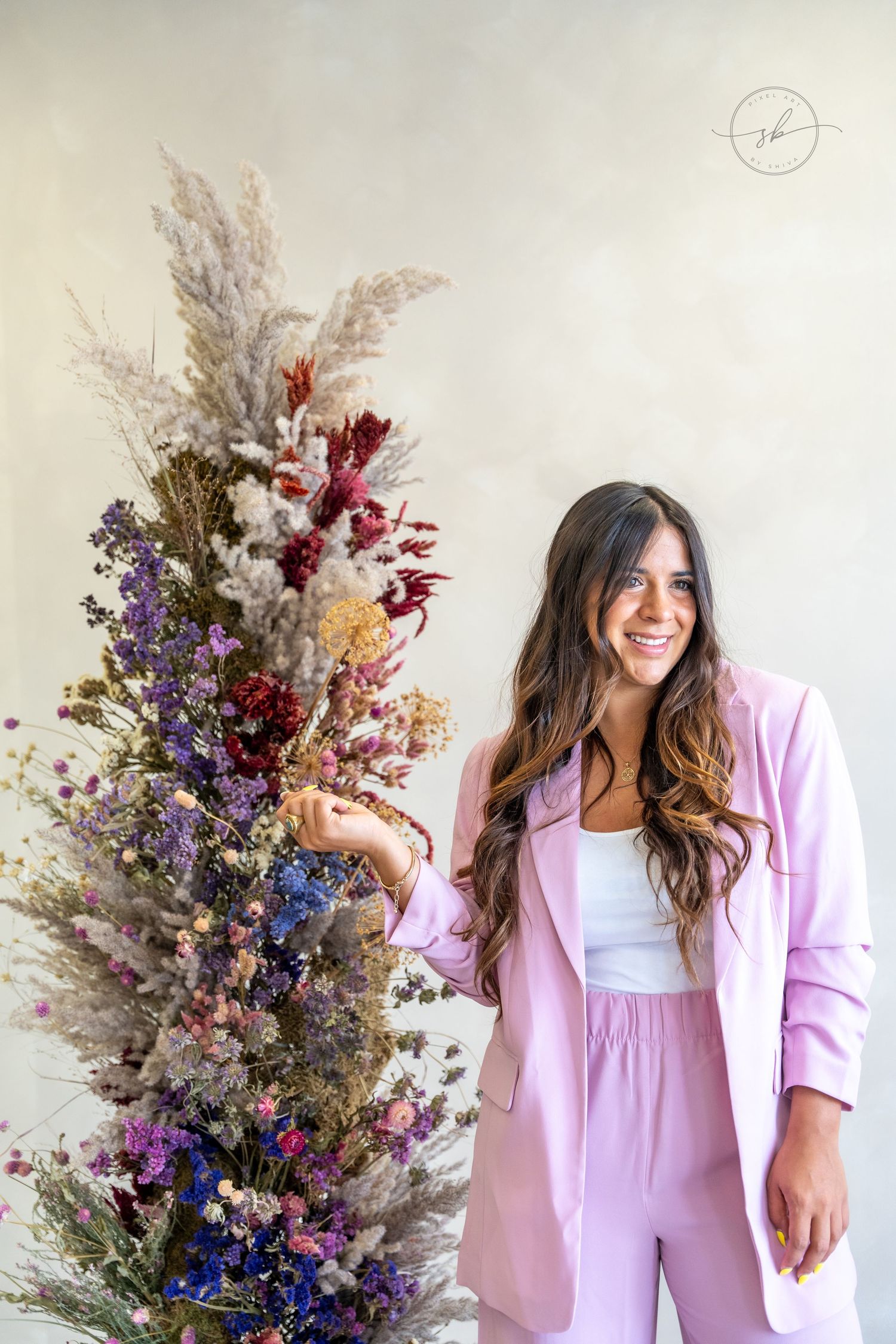 A bright dried floral arrangement featuring purple, red and yellow blooms next to pink professional attire.