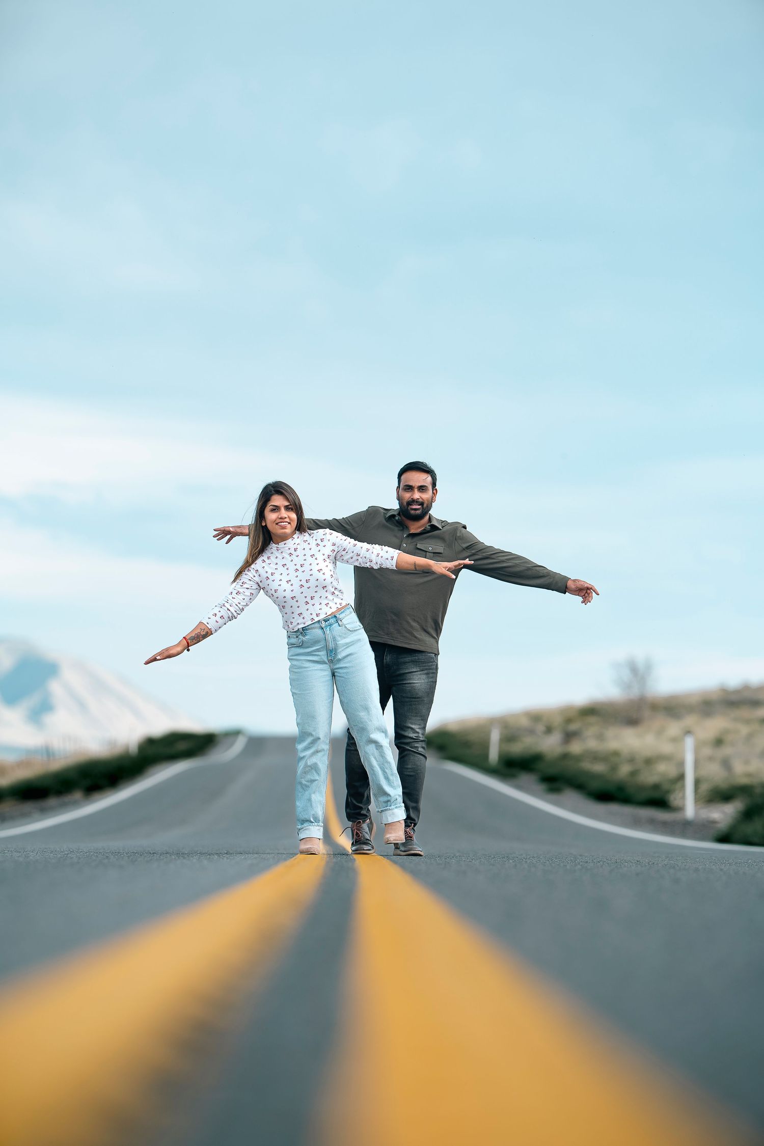 A playful couple balances with arms outstretched on a rural mountain road.