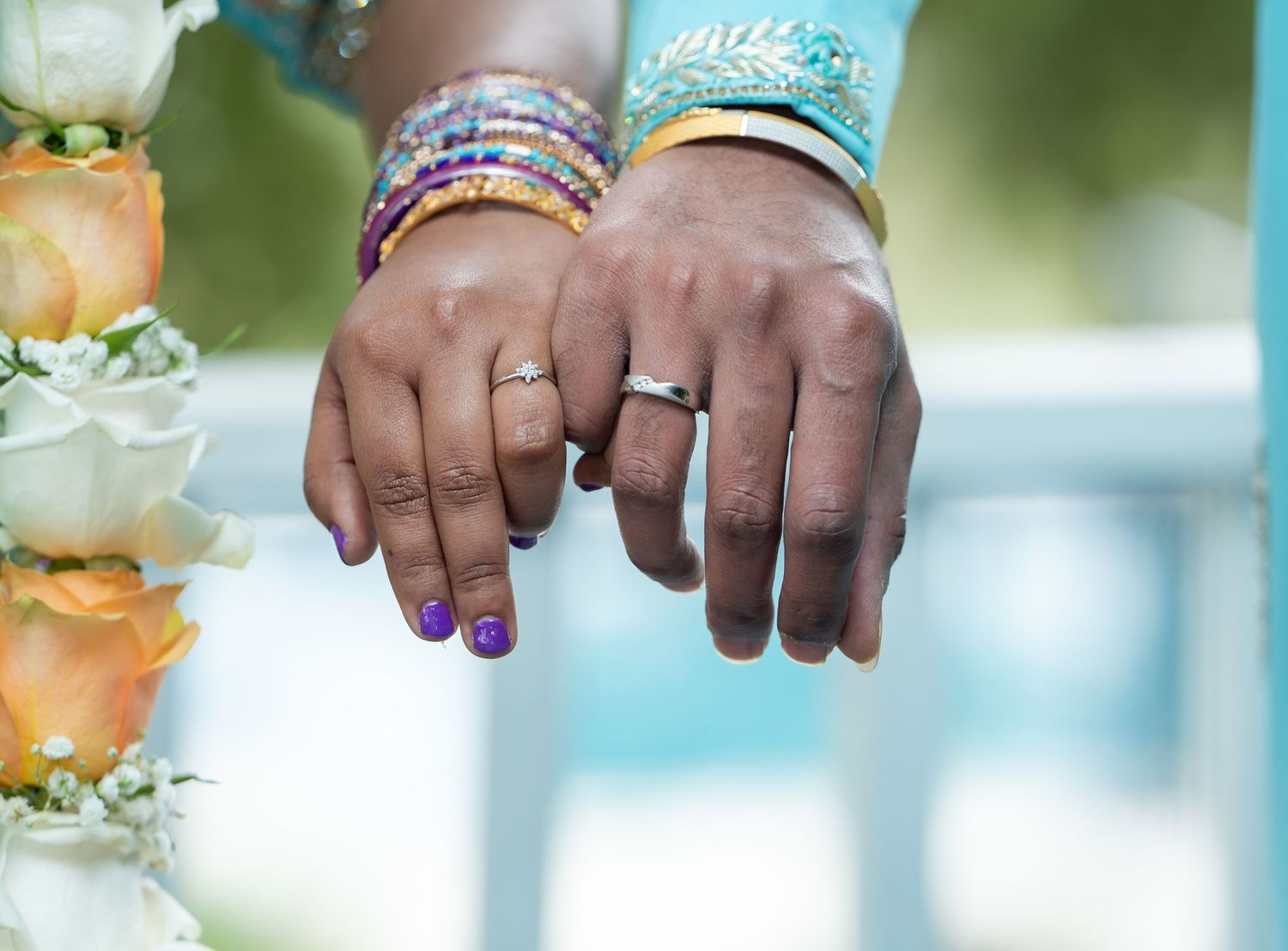 Close-up of newlyweds' hands showing wedding rings and colorful bridal bangles.