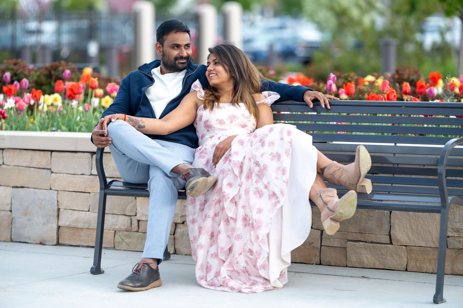 A couple sits together on a stone wall near colorful tulip gardens.