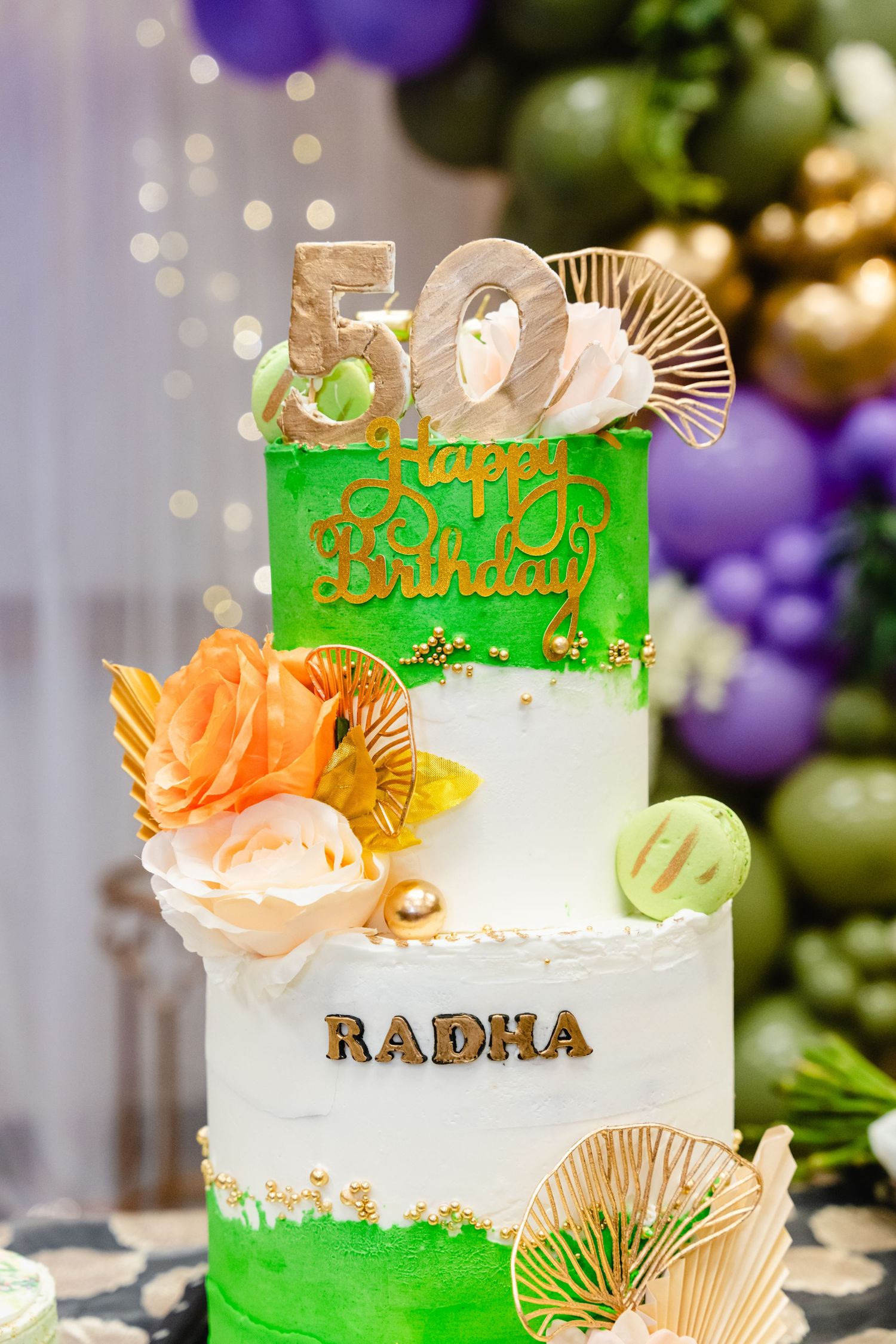 Elegant green and white birthday cake decorated with gold accents and 'RADHA' lettering, featuring peach-colored flowers.