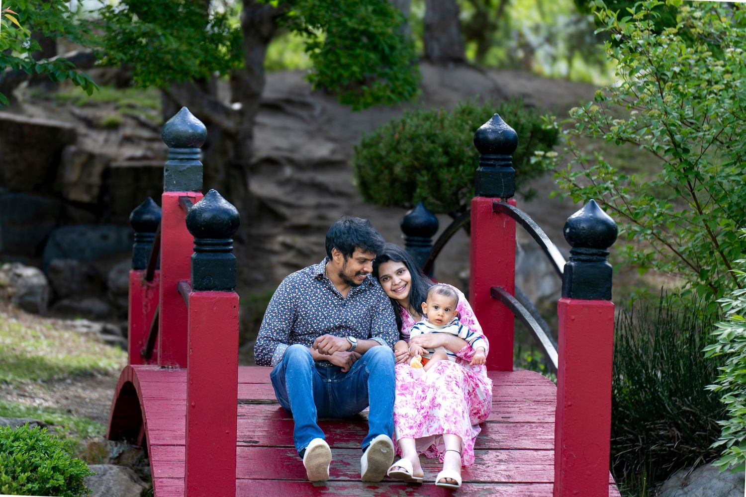 A family sits together on red painted steps surrounded by greenery.