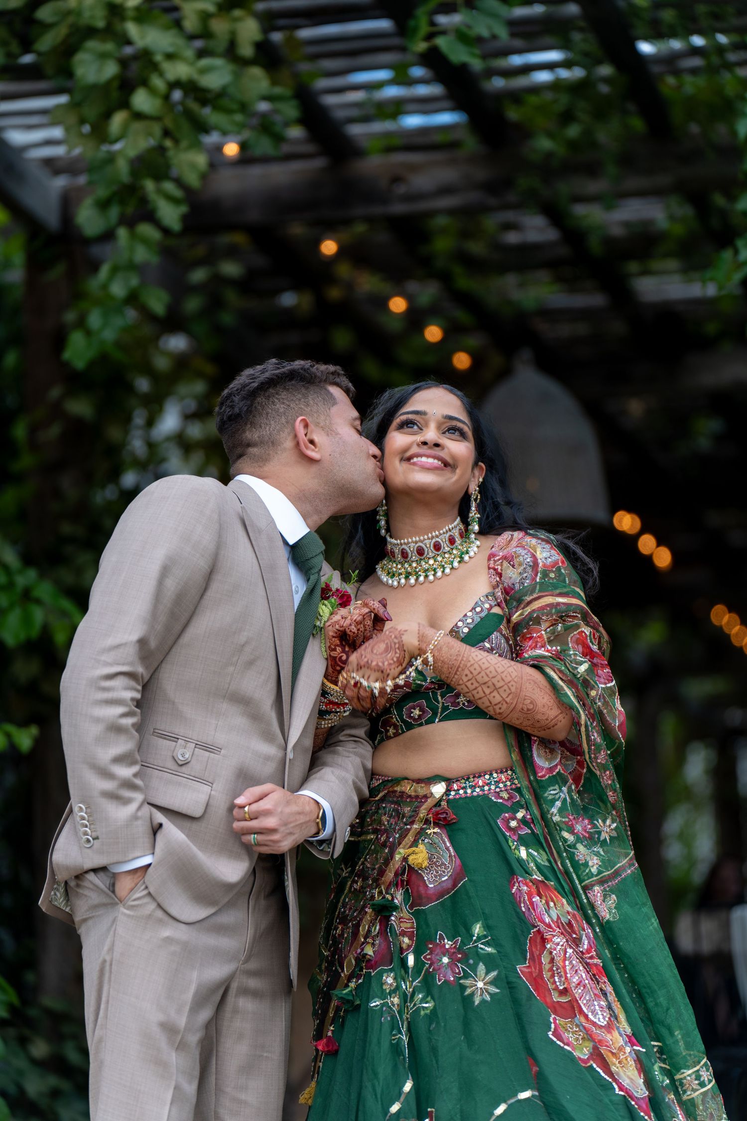 Intimate moment shared between couple against backdrop of garden trellis with string lights.