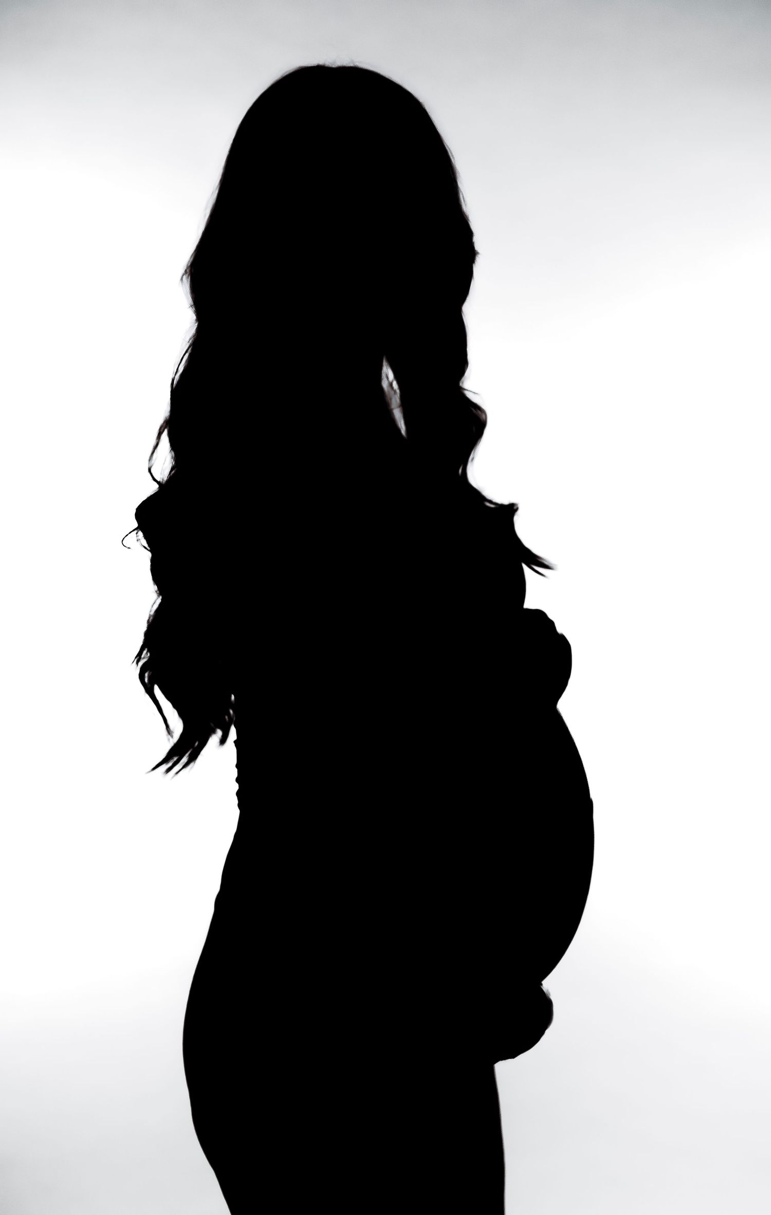 Silhouette profile of pregnant woman highlighting baby bump against white background.