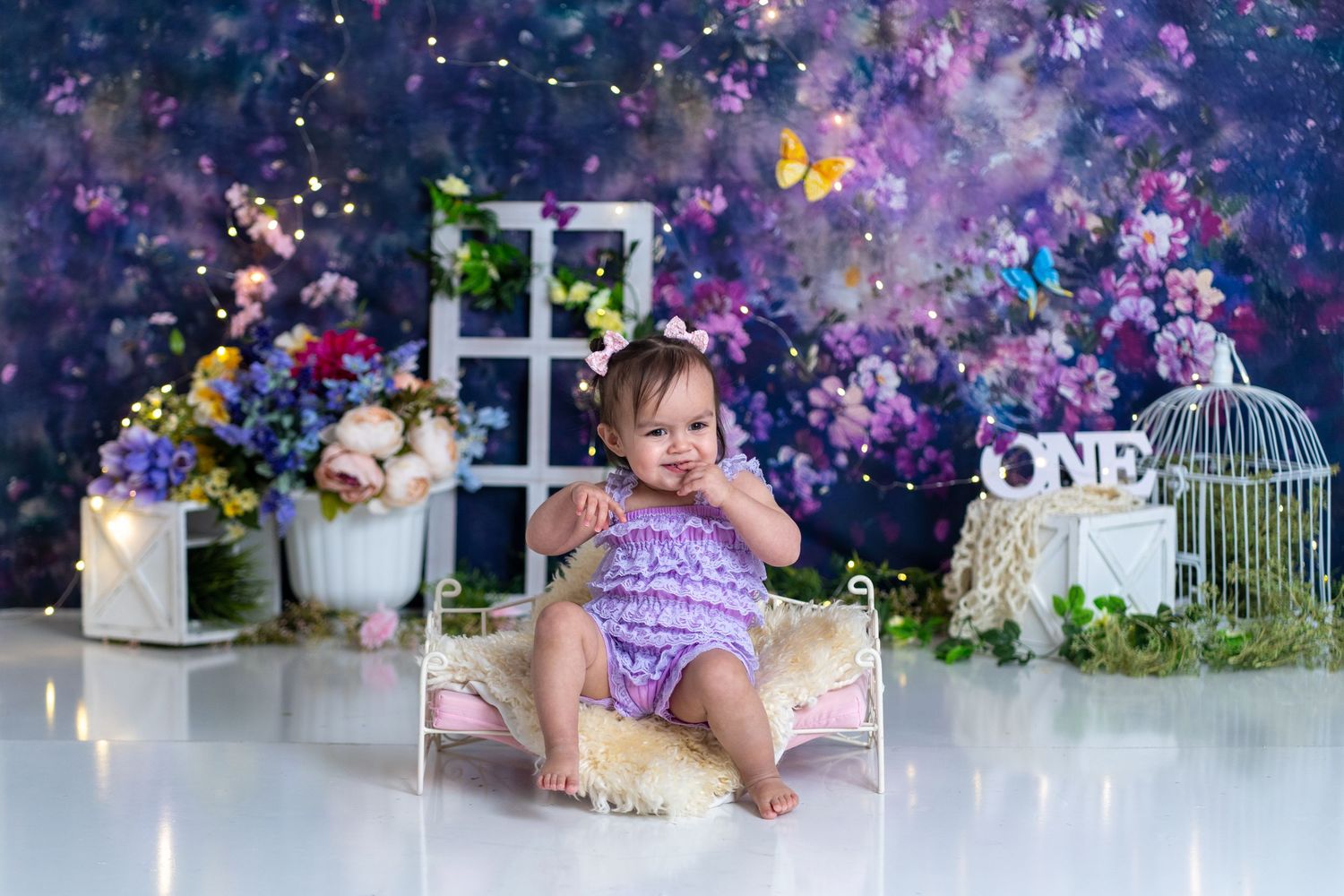 Purple themed cake smash photo with butterfly decorations and dreamy garden backdrop.