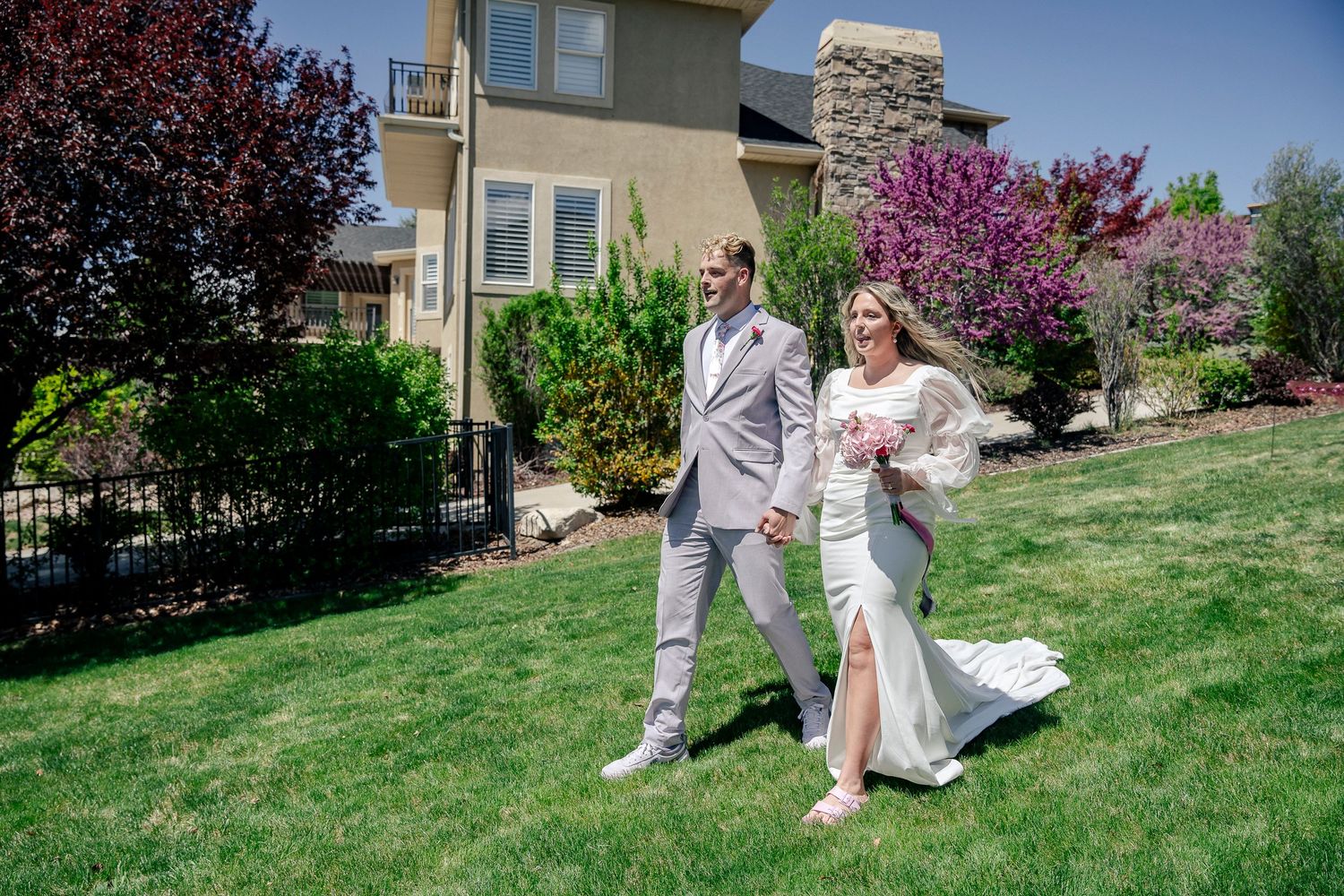 A couple poses on their wedding day with blooming trees and a modern house in the background.