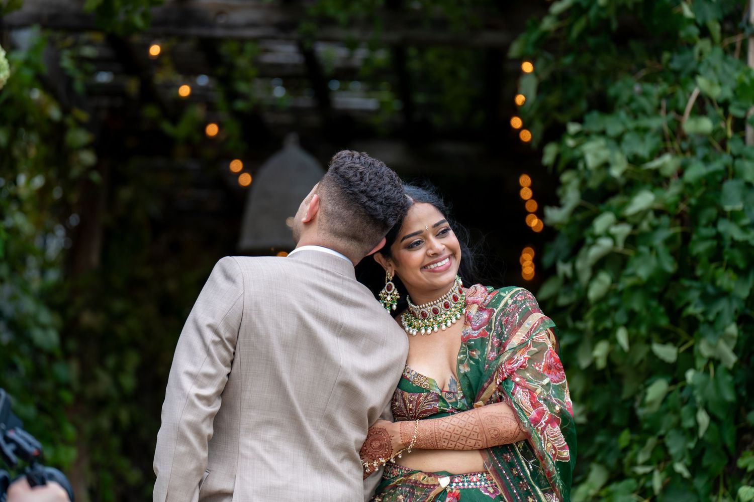 Romantic couple moment in garden setting with string lights and greenery.