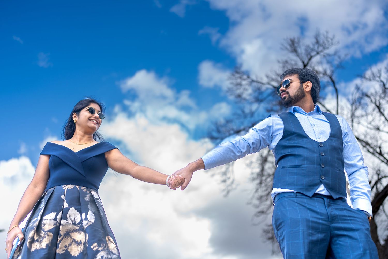 Couple in navy blue outfits holding hands against cloudy sky.