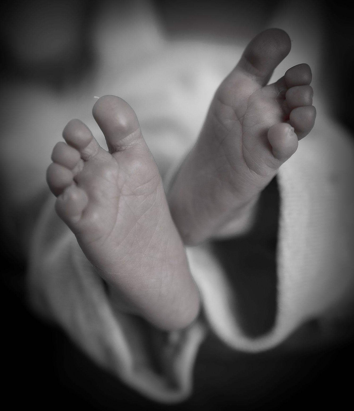 Black and white artistic photo of baby feet against soft fabric background.