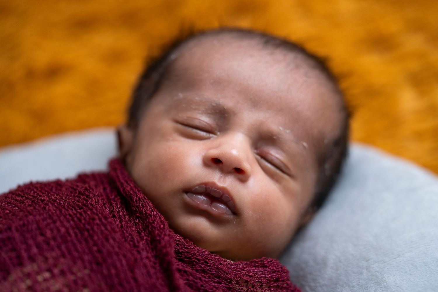 Sleeping peaceful baby wrapped in a burgundy knit blanket against orange background.