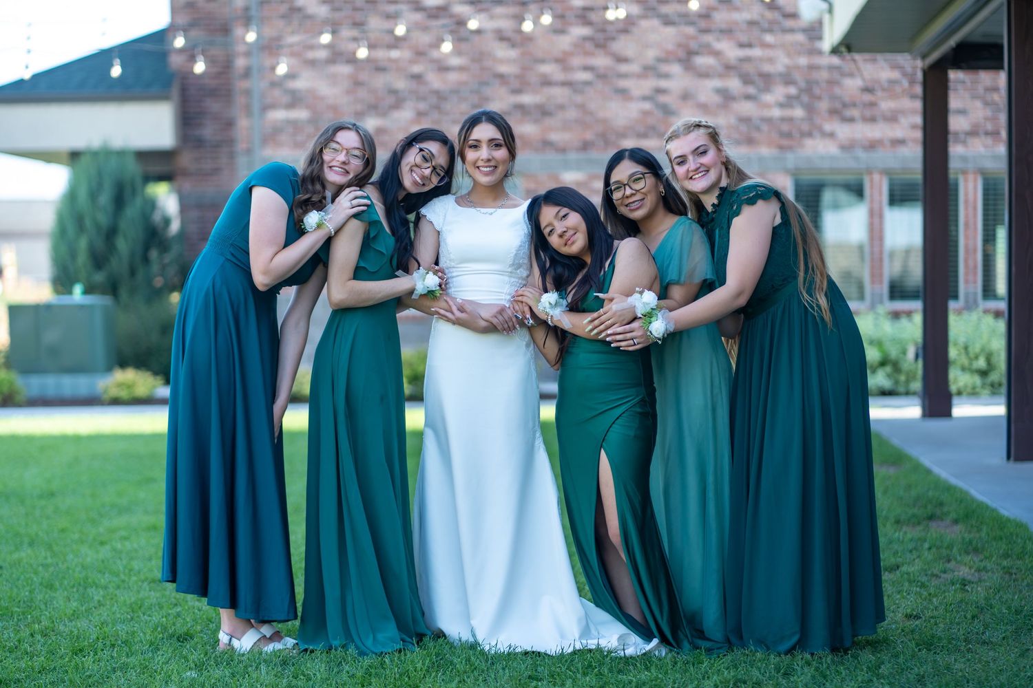 Wedding party in varying shades of teal dresses gathered around bride in white gown.