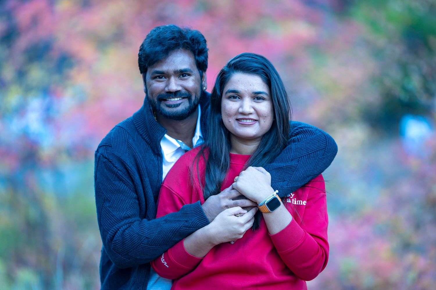 Couple embracing in casual winter wear against colorful autumn backdrop.