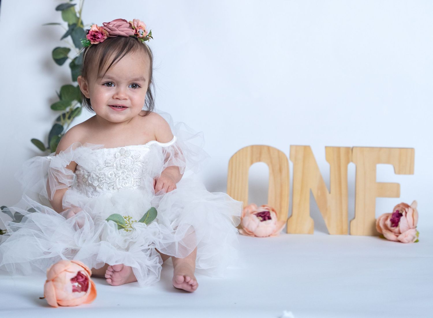 First birthday portrait with wooden ONE letters and floral decorations in white setting.
