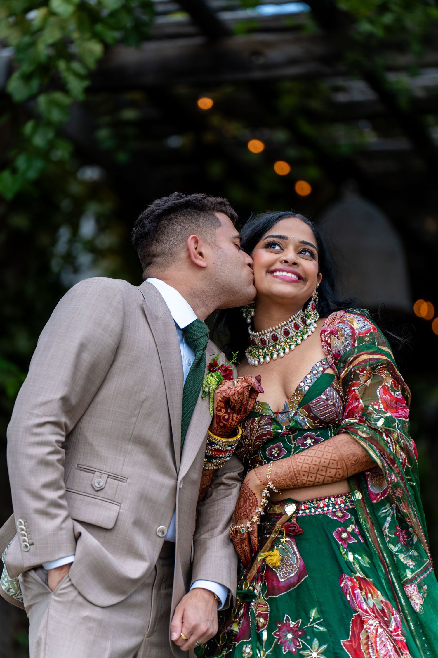 Romantic couple shares tender moment in garden setting with twinkling lights and lush greenery.