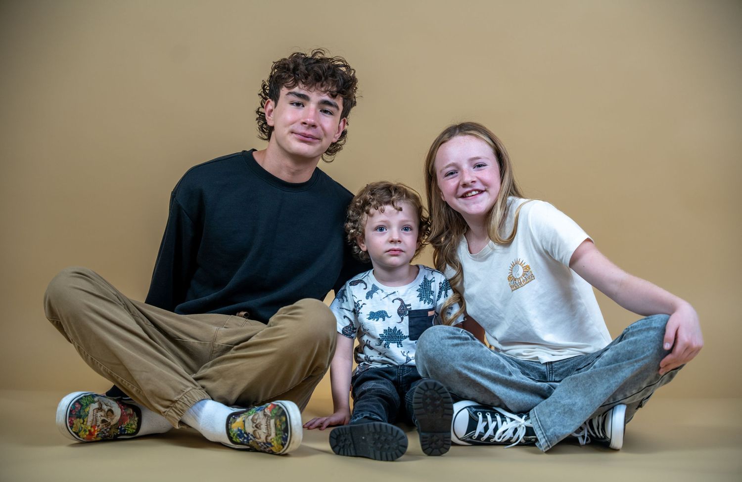Three siblings pose together for casual studio portrait.