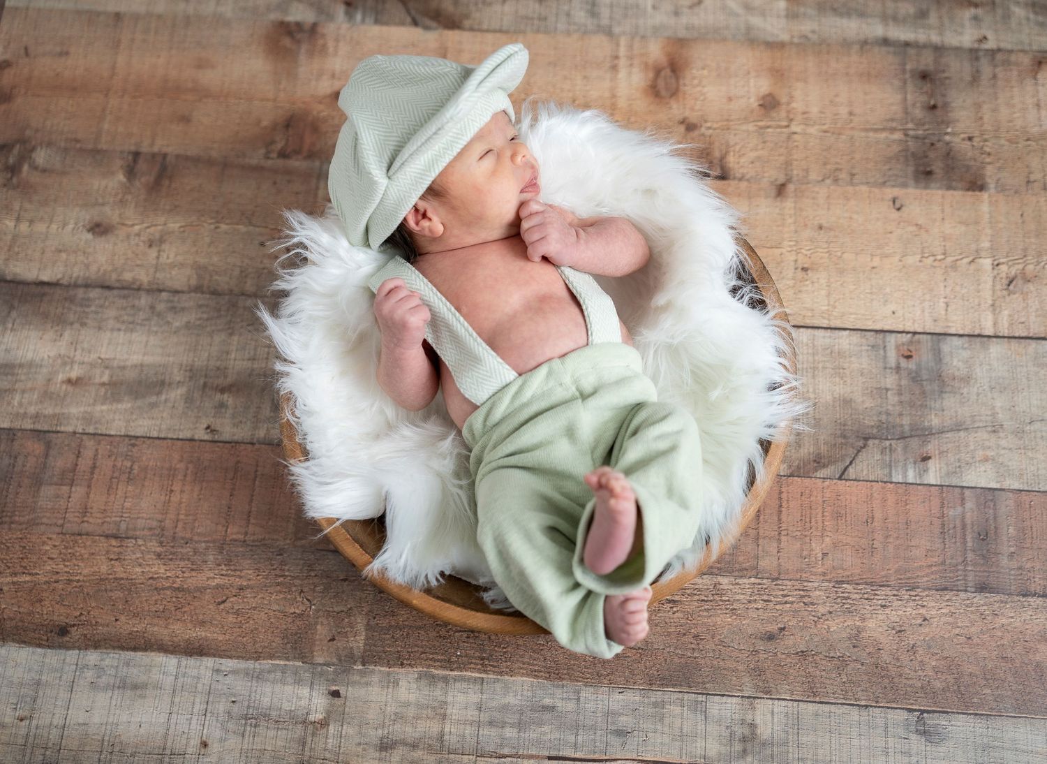 Newborn baby sleeping in rustic wooden bowl wearing mint green outfit.
