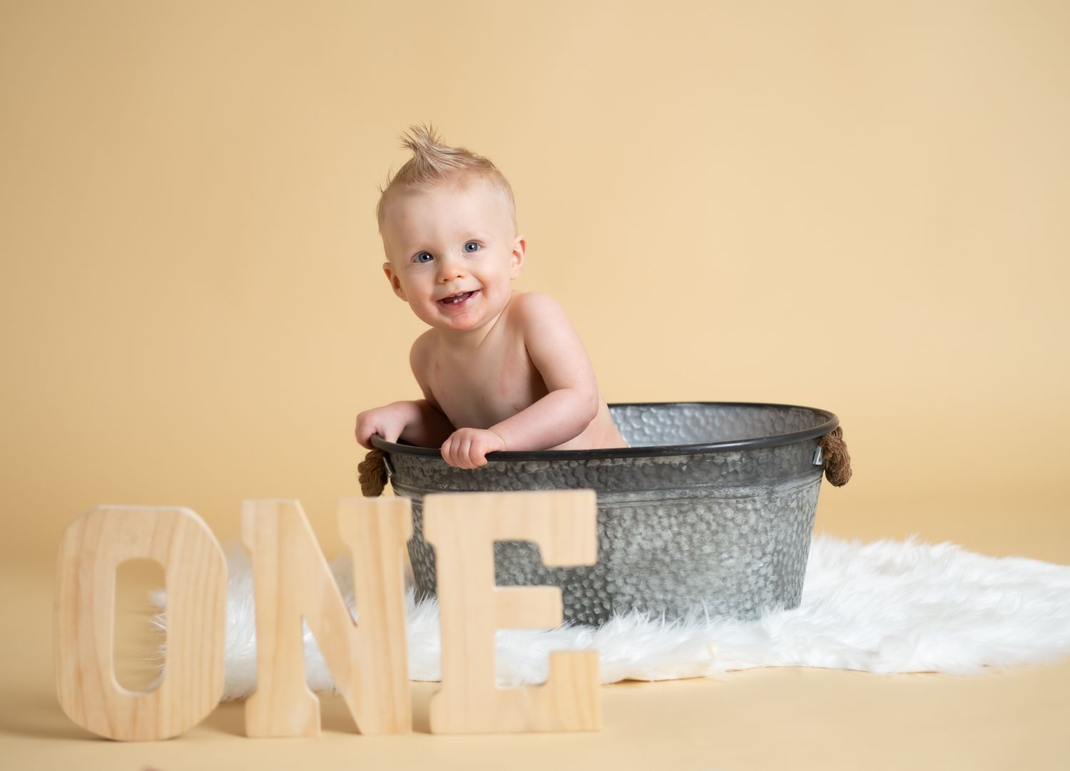 Baby photography setup with vintage metal tub and wooden ONE letters on cream background.