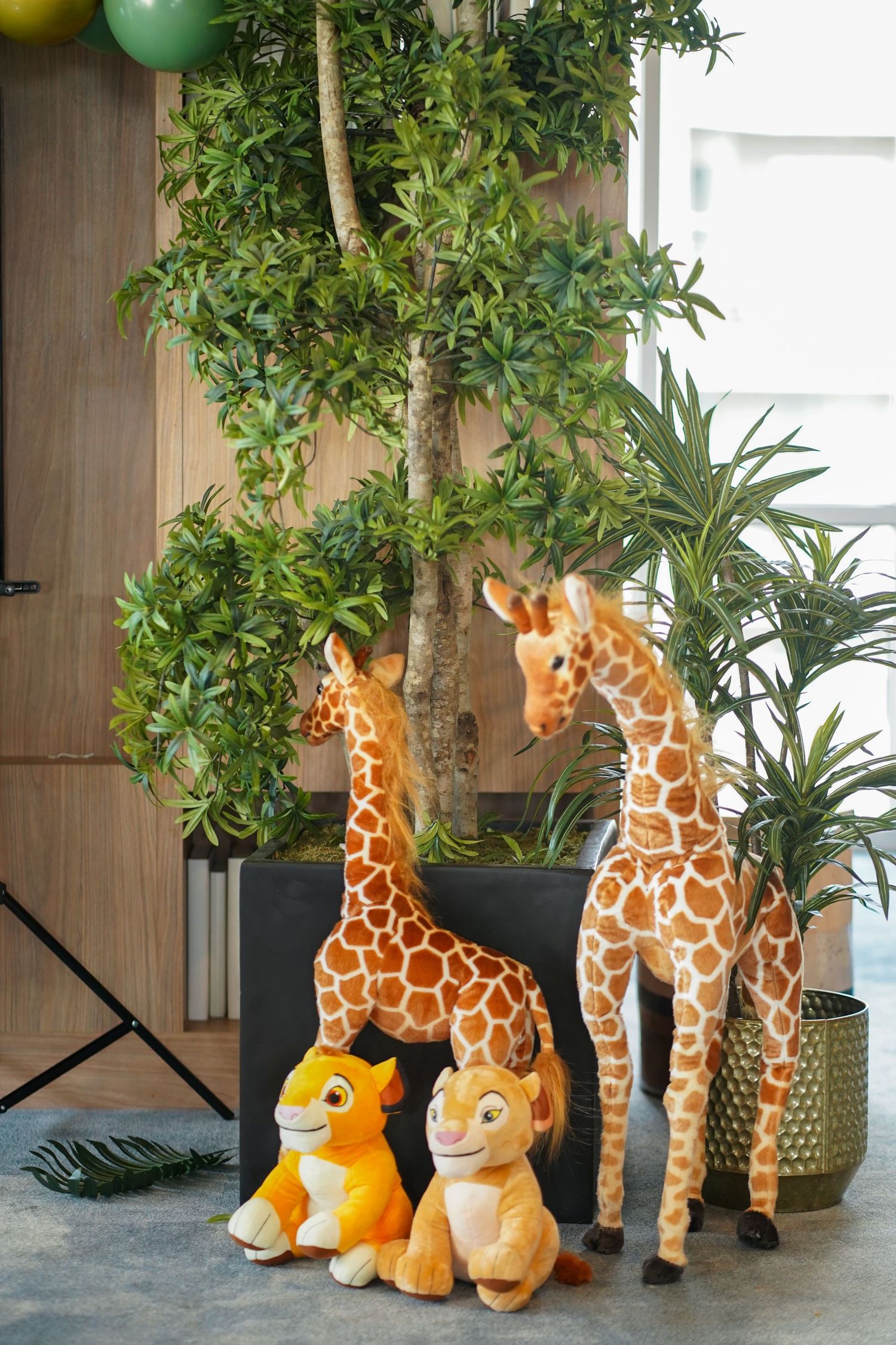 Safari-themed decorations featuring plush giraffes and lion toys beside indoor plants.