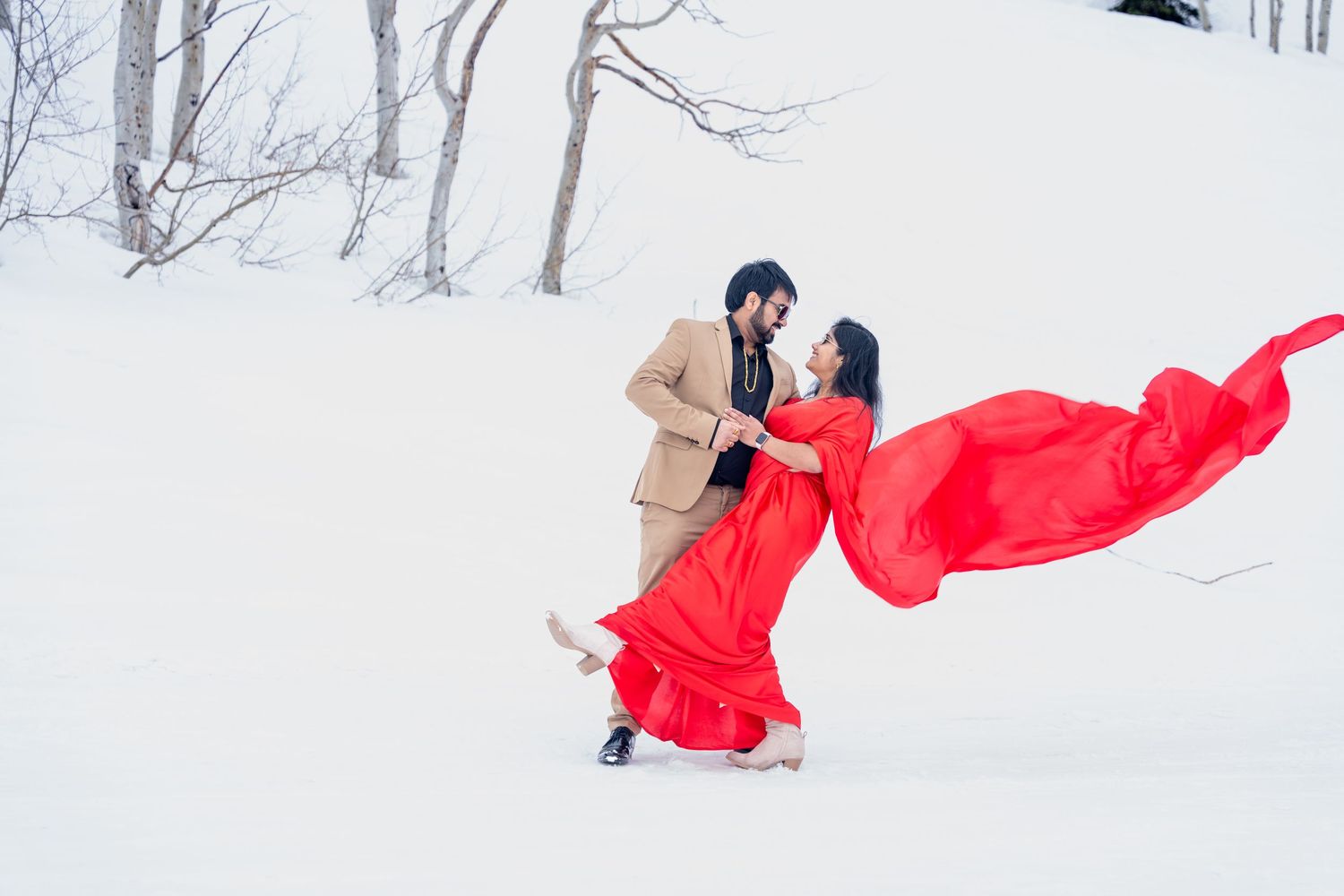 Winter engagement photo with flowing red dress against snowy landscape.